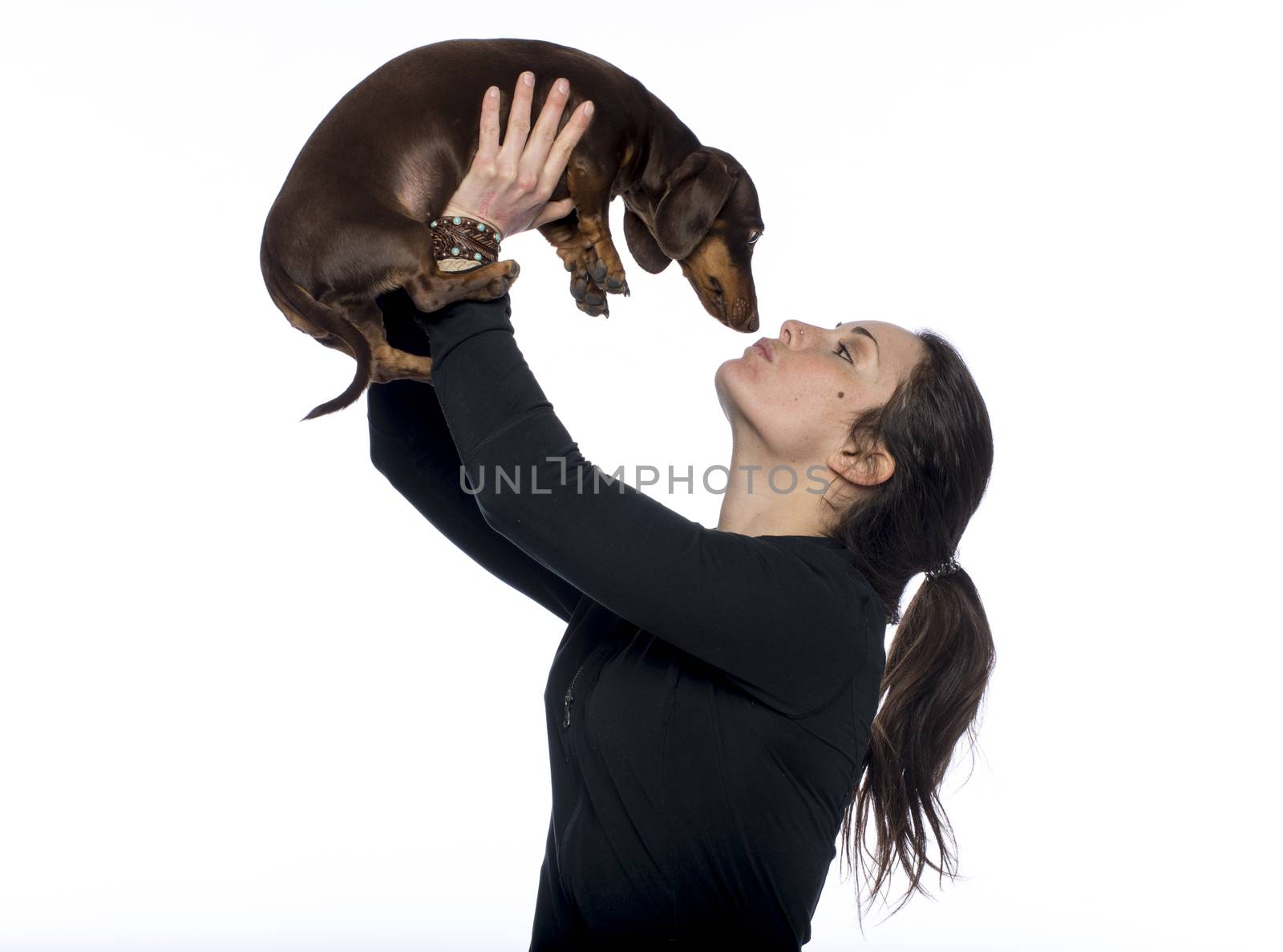 Caucasian brunette holds her dachshund dog in air giving it kiss