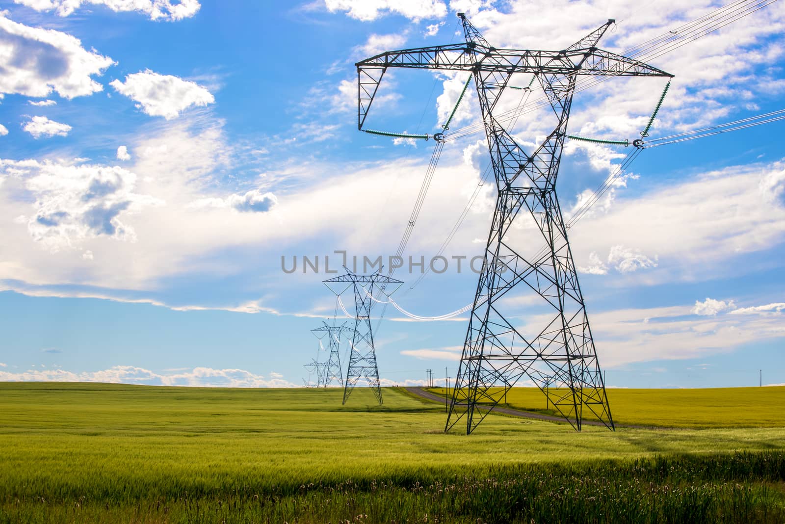 Power lines in a farm field on a sunny day with clouds