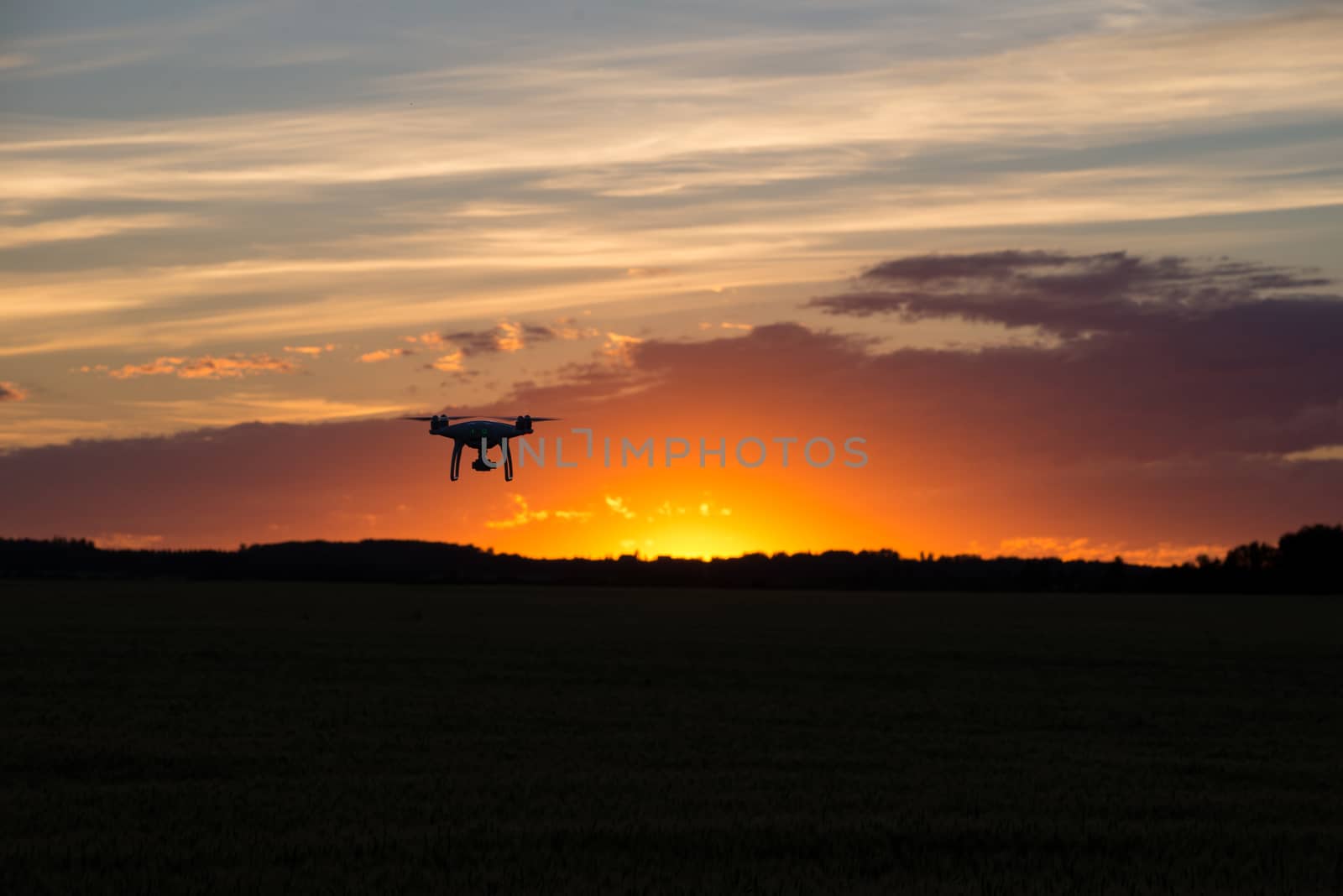 Drone silhouetted against orange sunset taking video