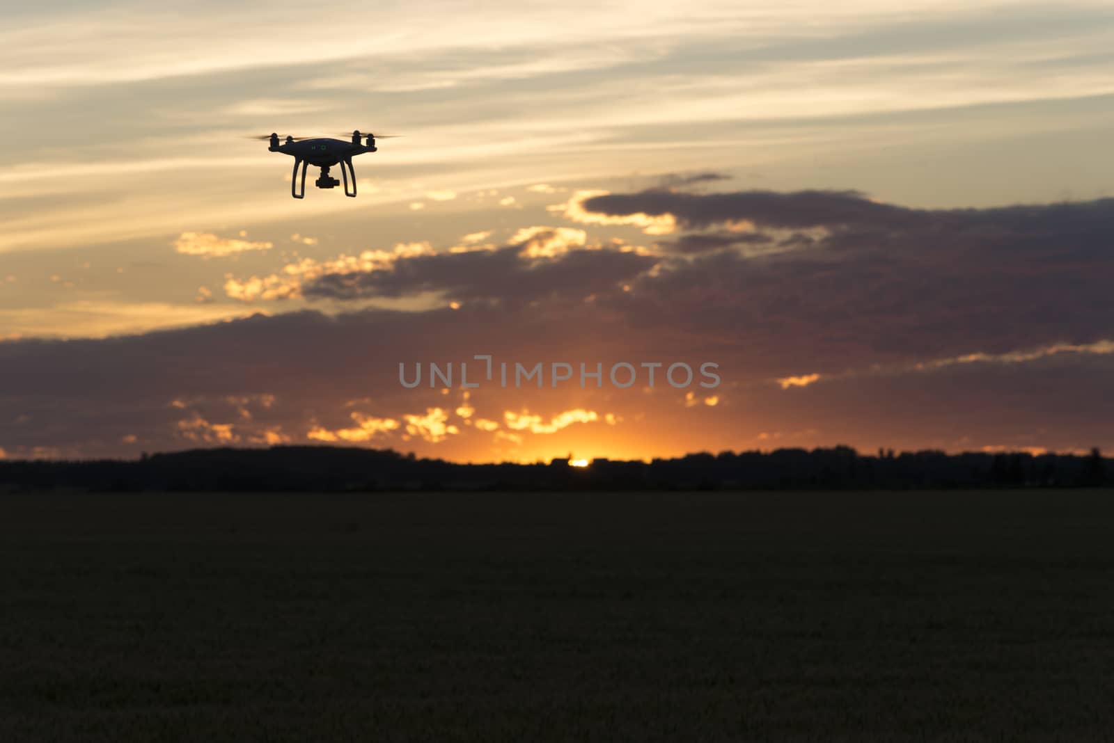 Drone silhouetted against orange sunset taking video