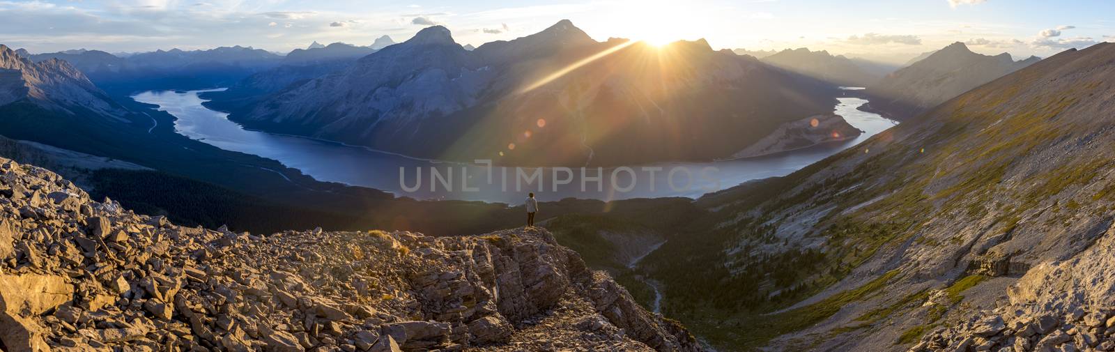 Girl watching sunset from peak of mountain above a lake.