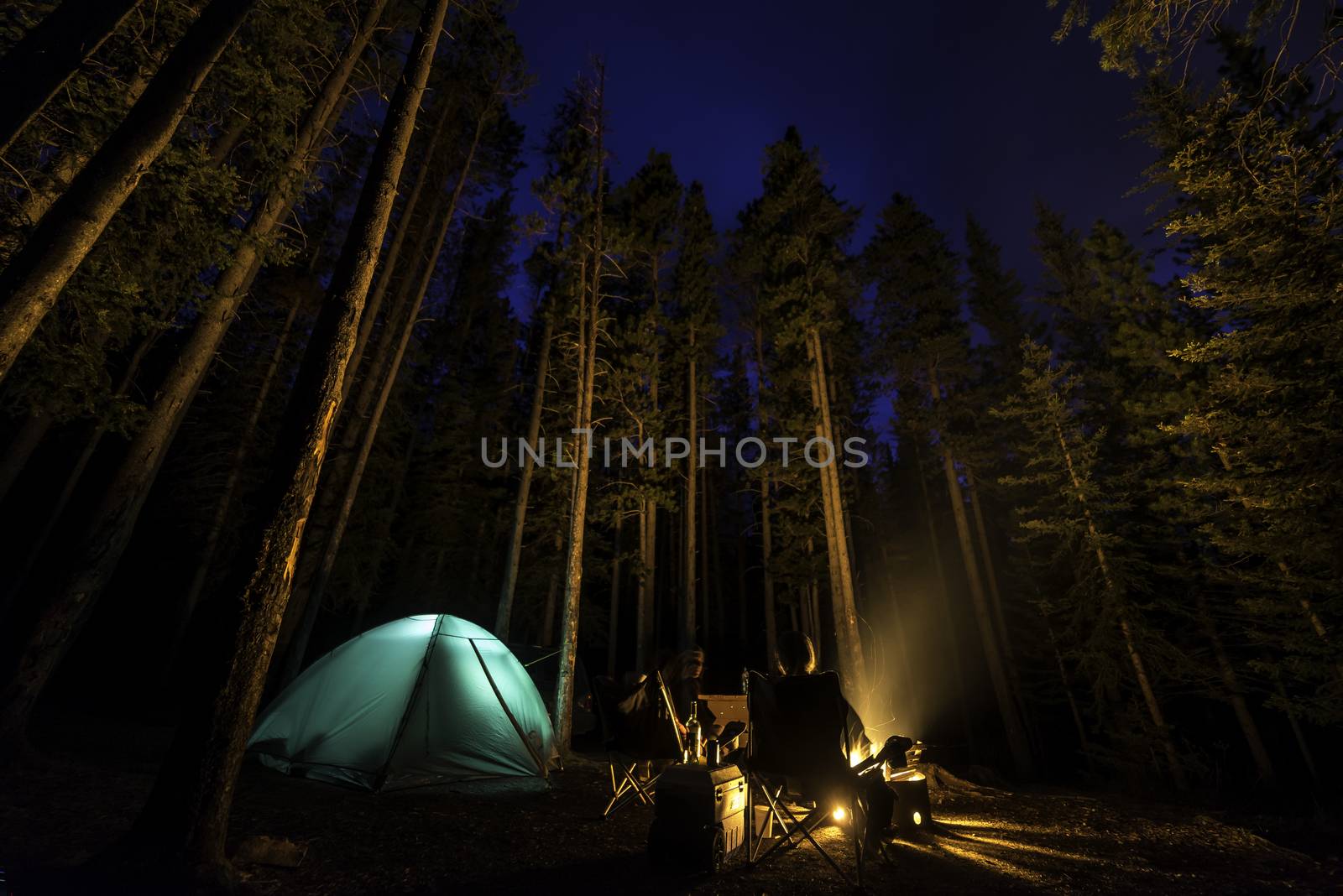 Two people camping in the forest with a fire by TSLPhoto