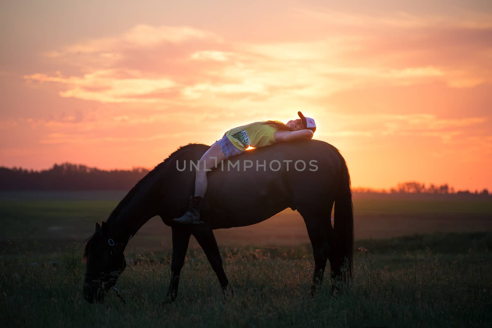 Girl lying on her horse without a sadle relaxing while it eats grass