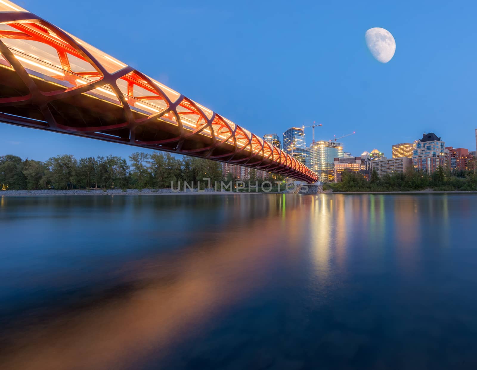Bridge over water in front of buildings with moon blue hour