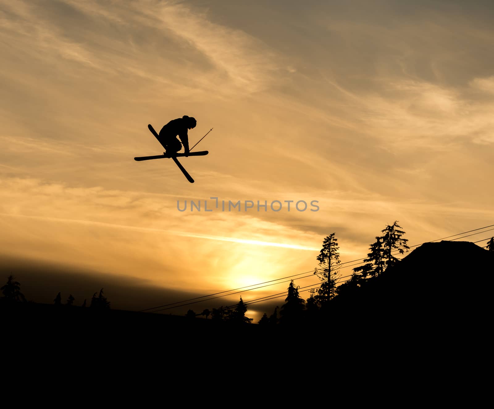 silhouette of skier doing grab off a jump in the sunset