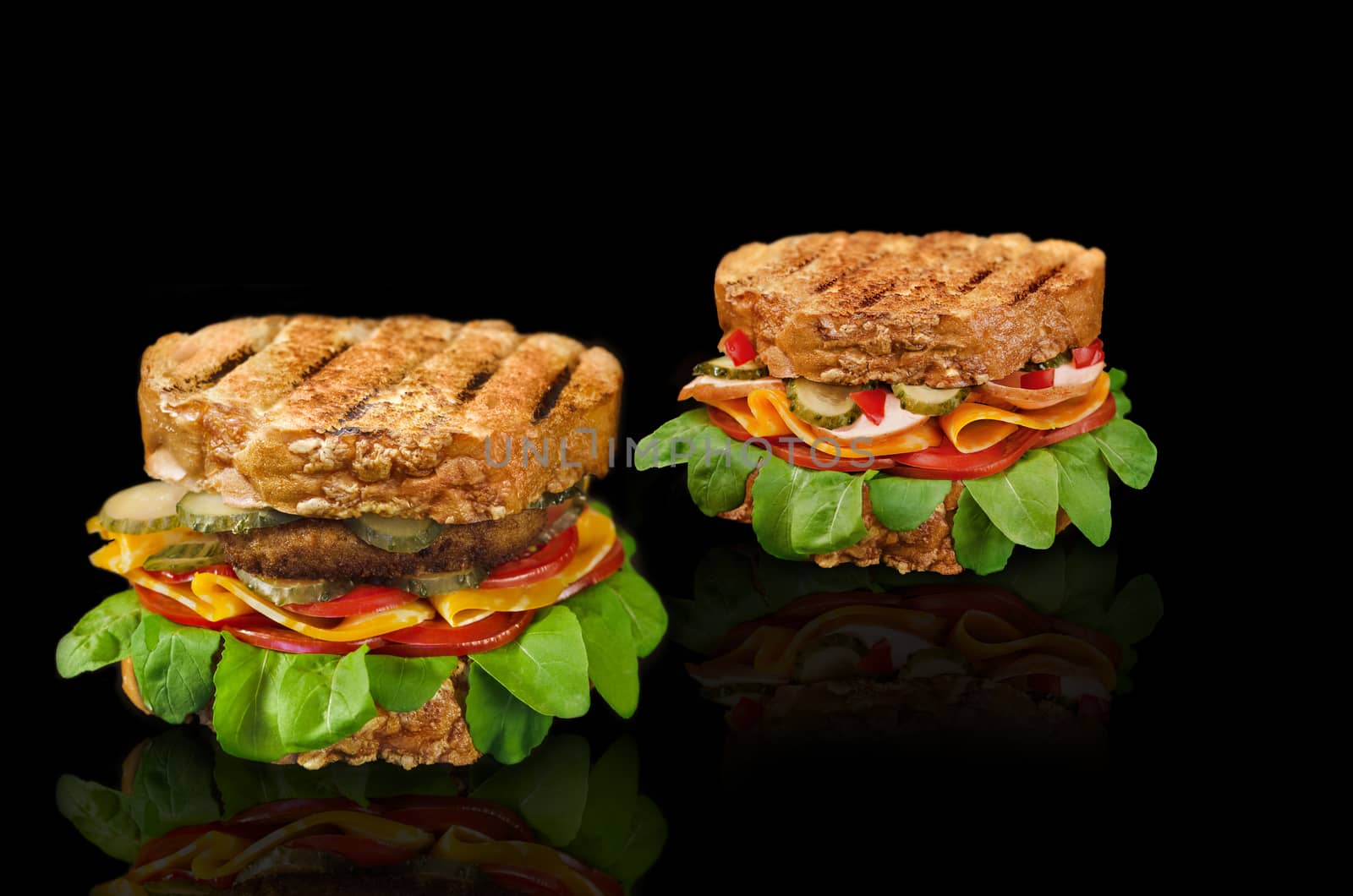 Two sandwiches with various fillings on a black background, with a cutlet, cheese, tomatoes, ham, cucumbers and herbs.