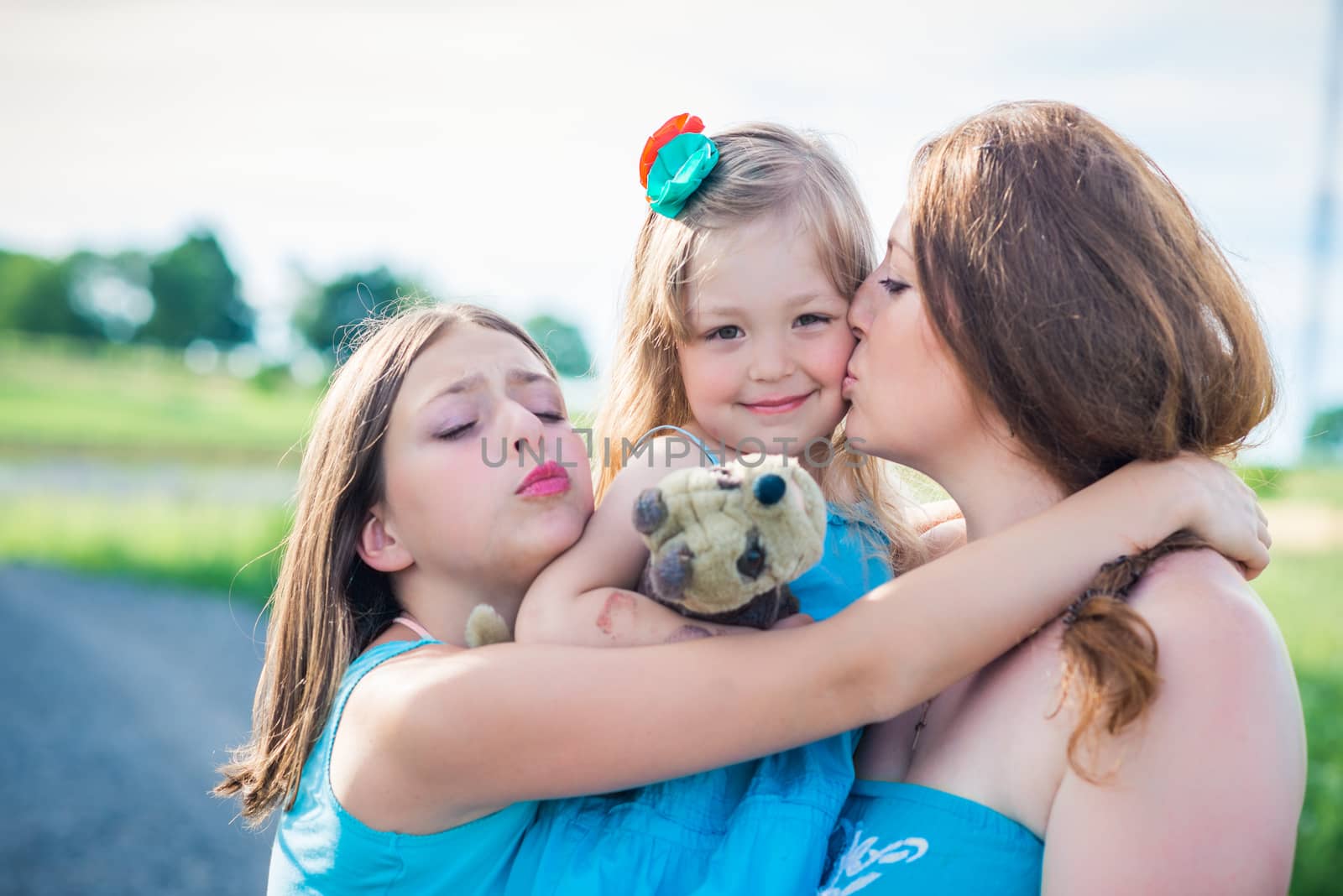 portrait of mother and two daughters. mother kissing daughter
