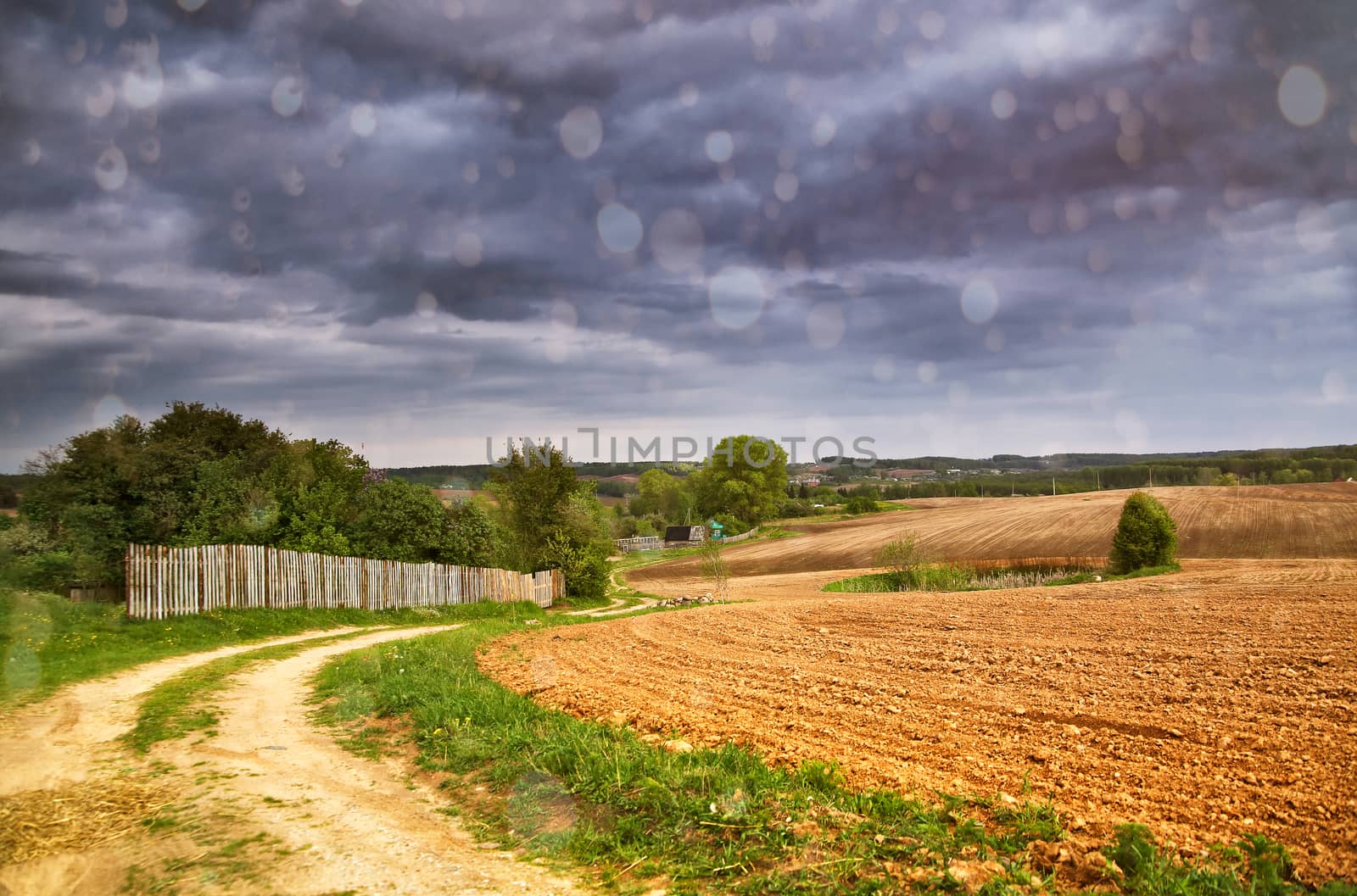 Rain and spring storm clouds above country road. Village and arable land field in spring