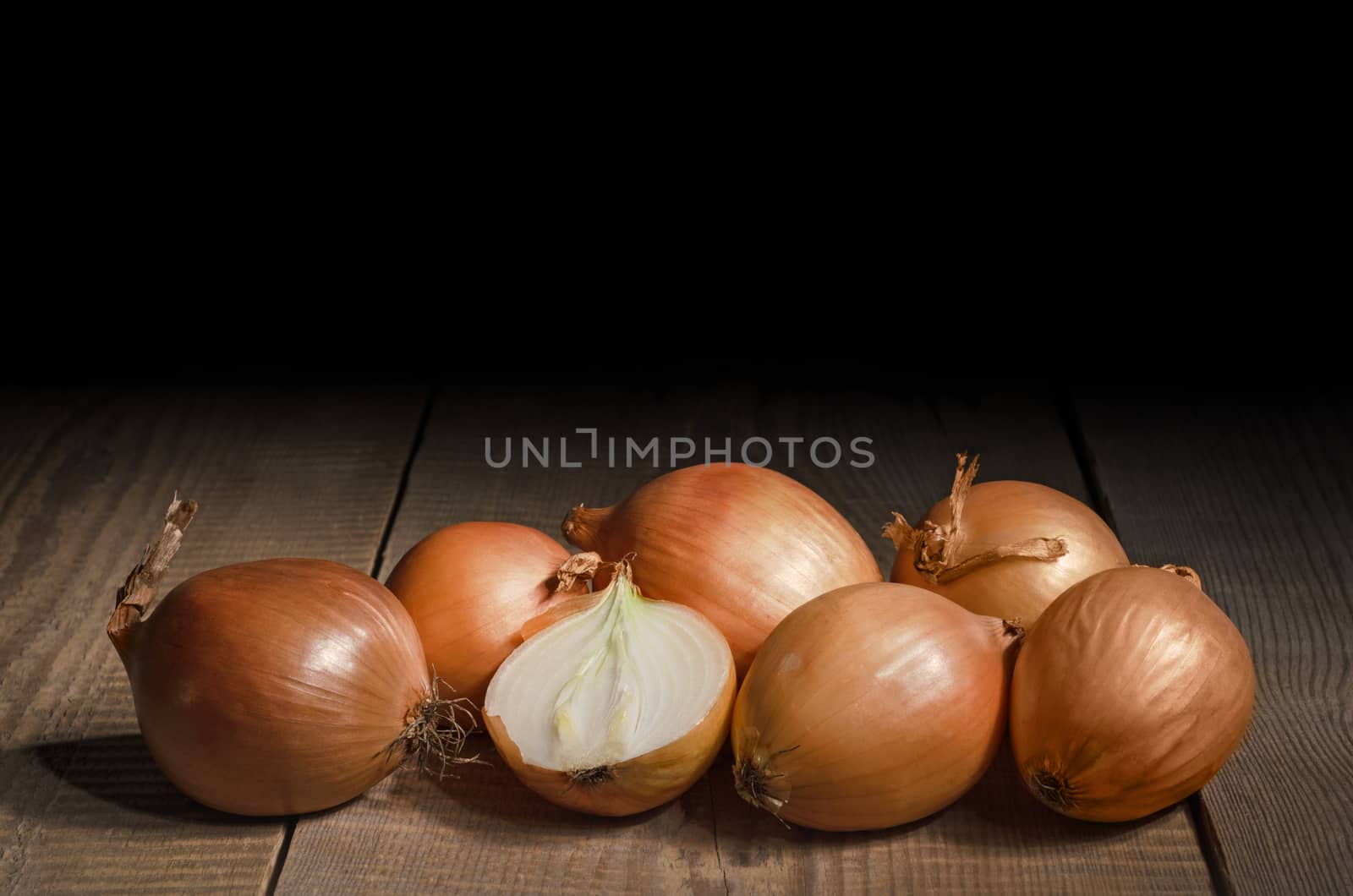 The onion lies on an old wooden table and a black background. by Gaina