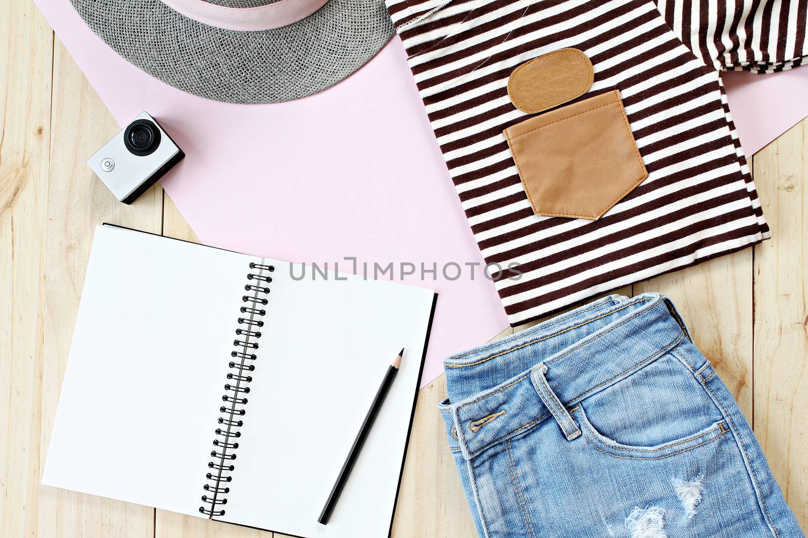 Fashion concept : Lady's outfit with jeans short, blank notebook paper and action camera on wooden background, casual outfit for teenage girls