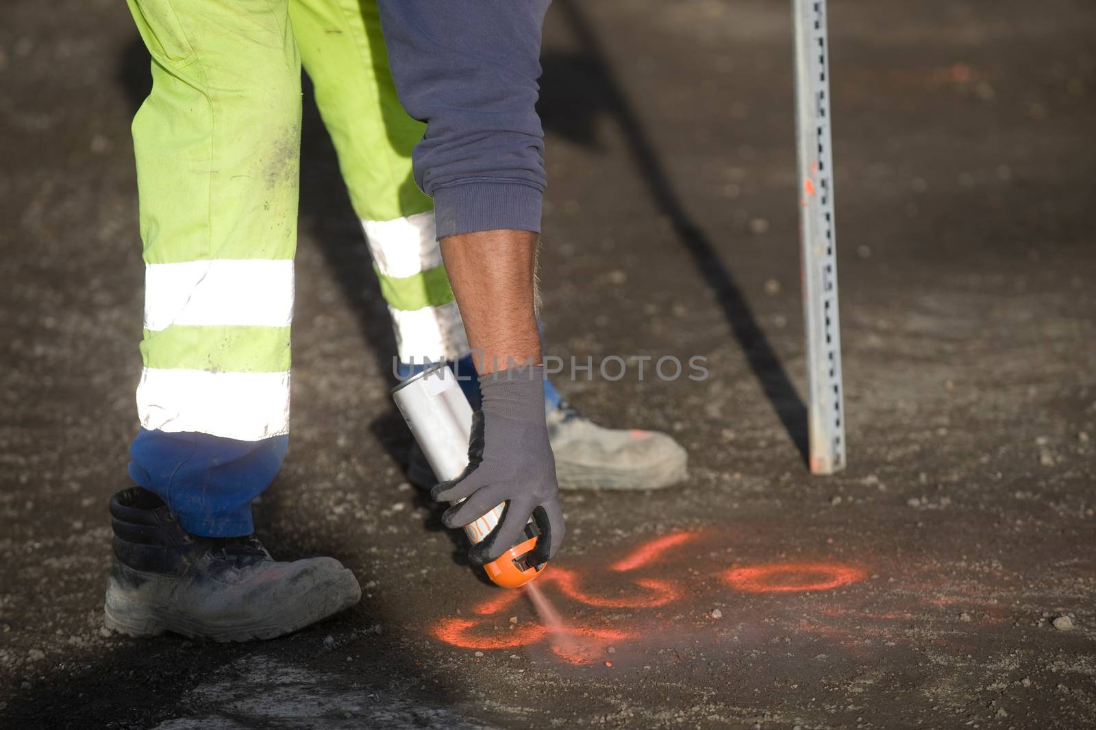Worker marks a spot on asphalt with florescent spray paint in preparation for widening a road