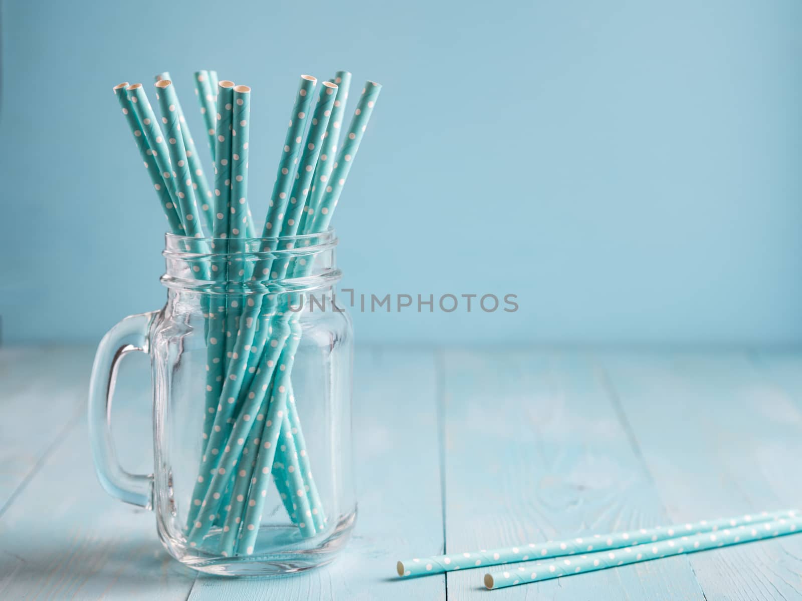 Mason jars with blue paper straws on blue wooden background. Ideal for summer drinks and smoothies. Copy space