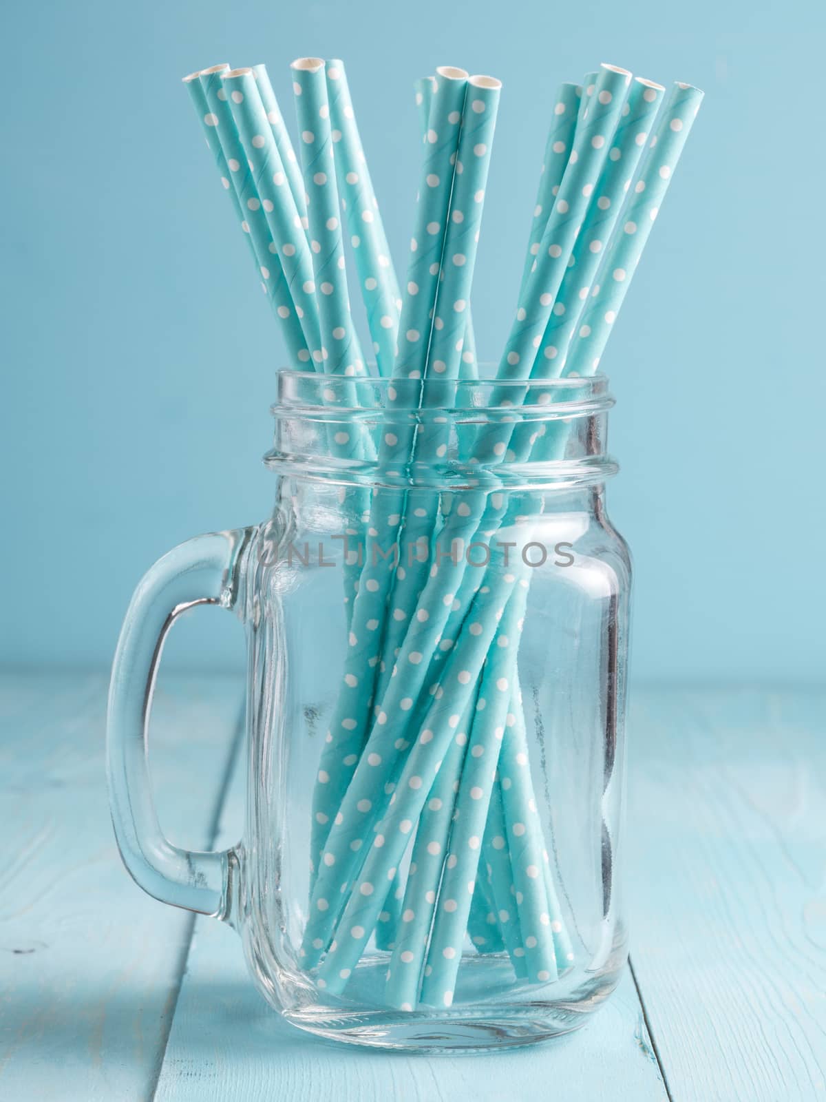 Mason jars with blue paper straws on blue wooden background. Ideal for summer drinks and smoothies. Vertical