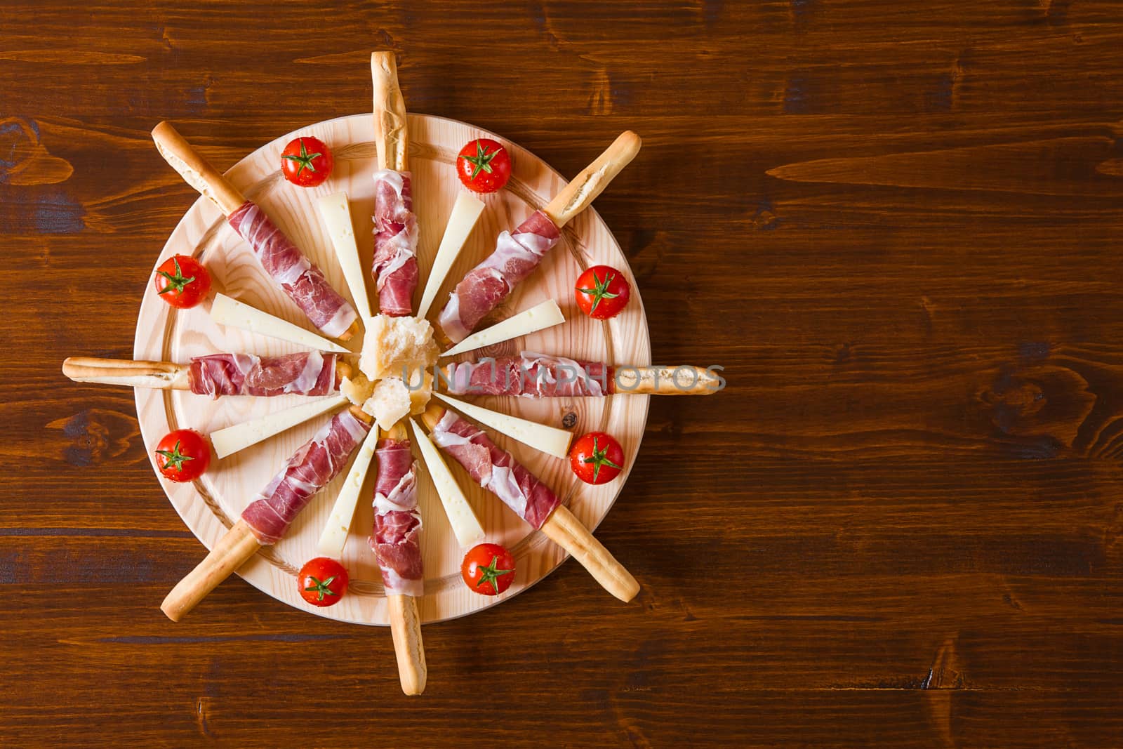 Chopping board with ham rolled in bread-sticks cheese and cherry tomatoes seen from above