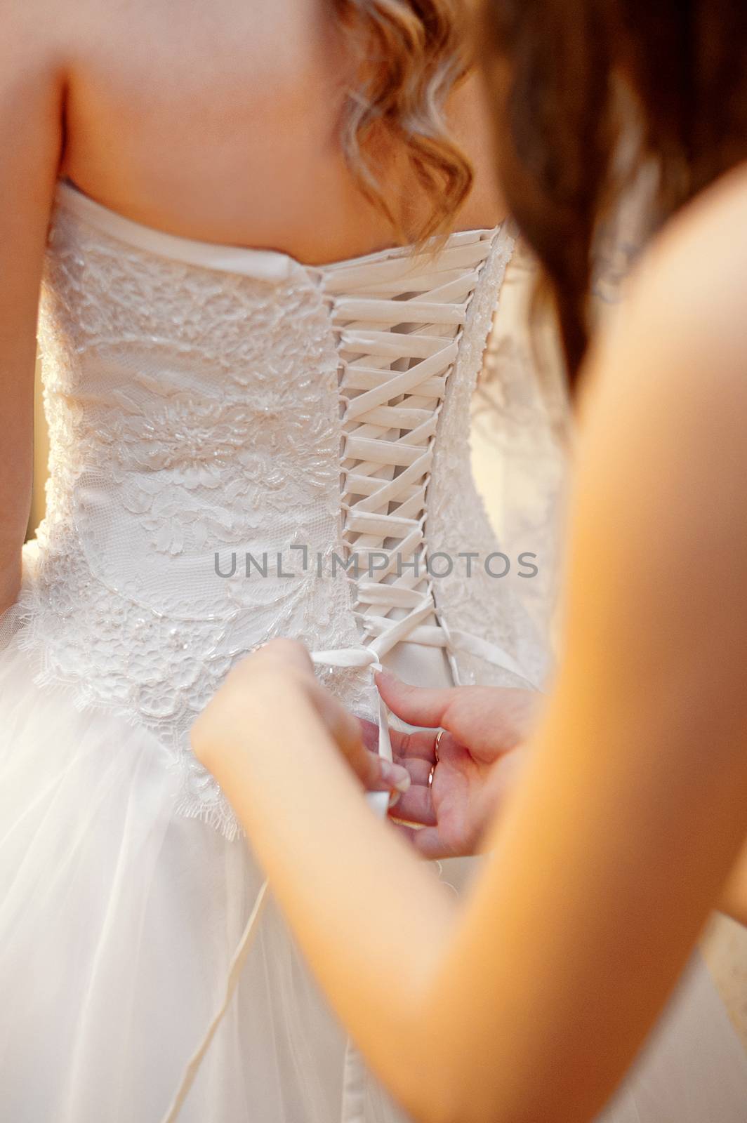 bridesmaid helps the bride to wear dress.