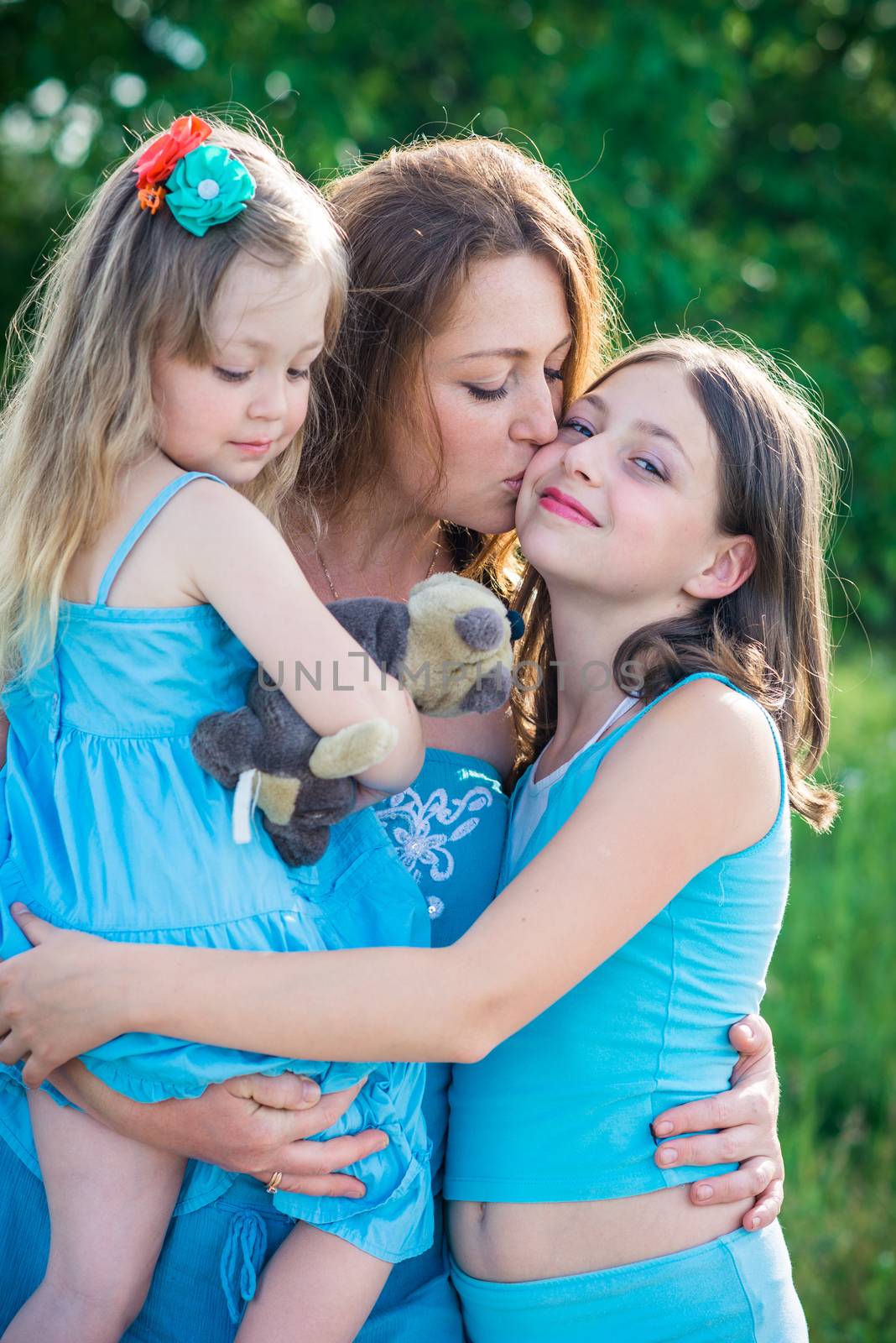 portrait of mother and two daughters. mother kissing daughter