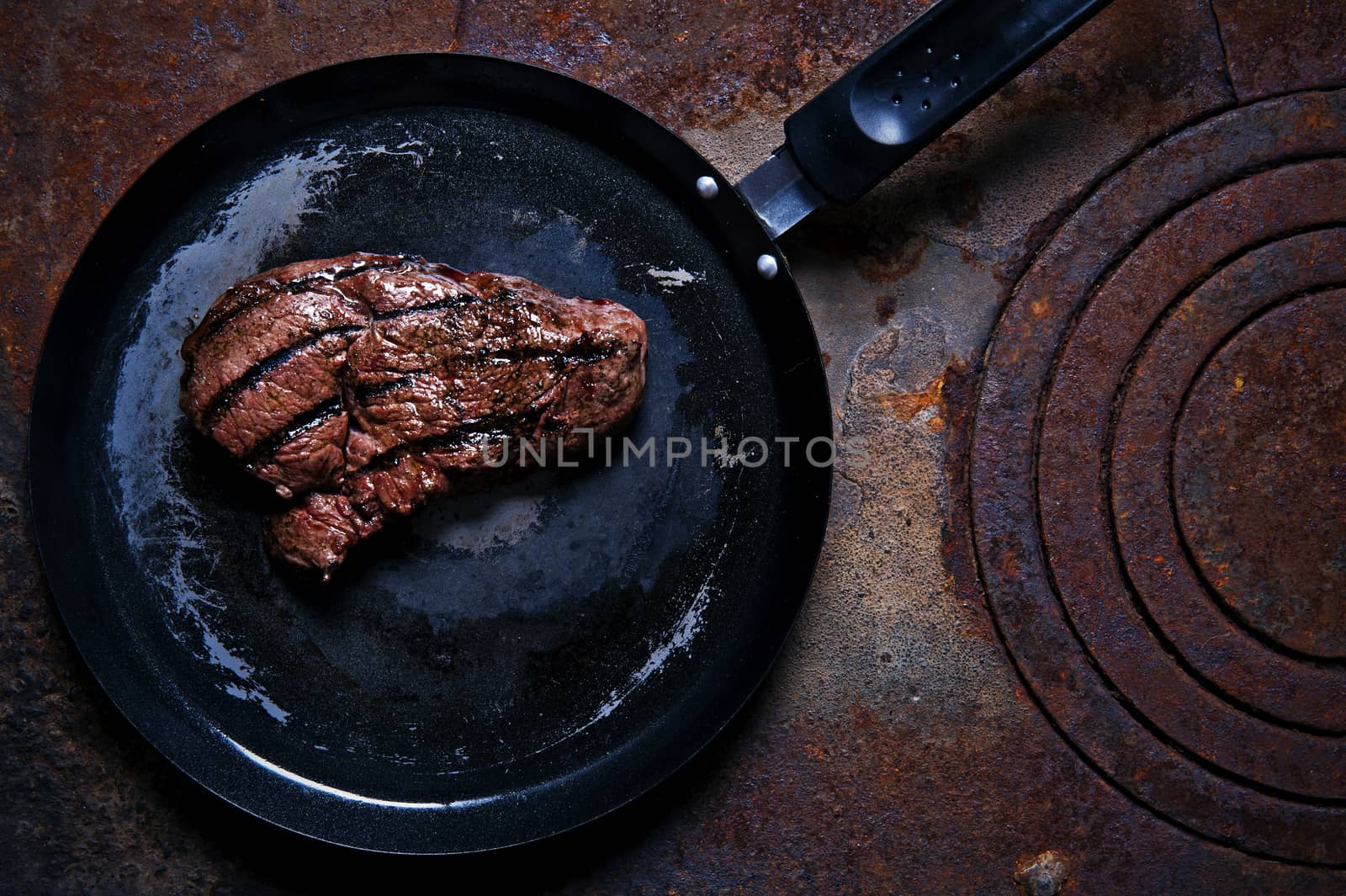Beef steak in a frying pan standing on the rusty burner by Michalowski