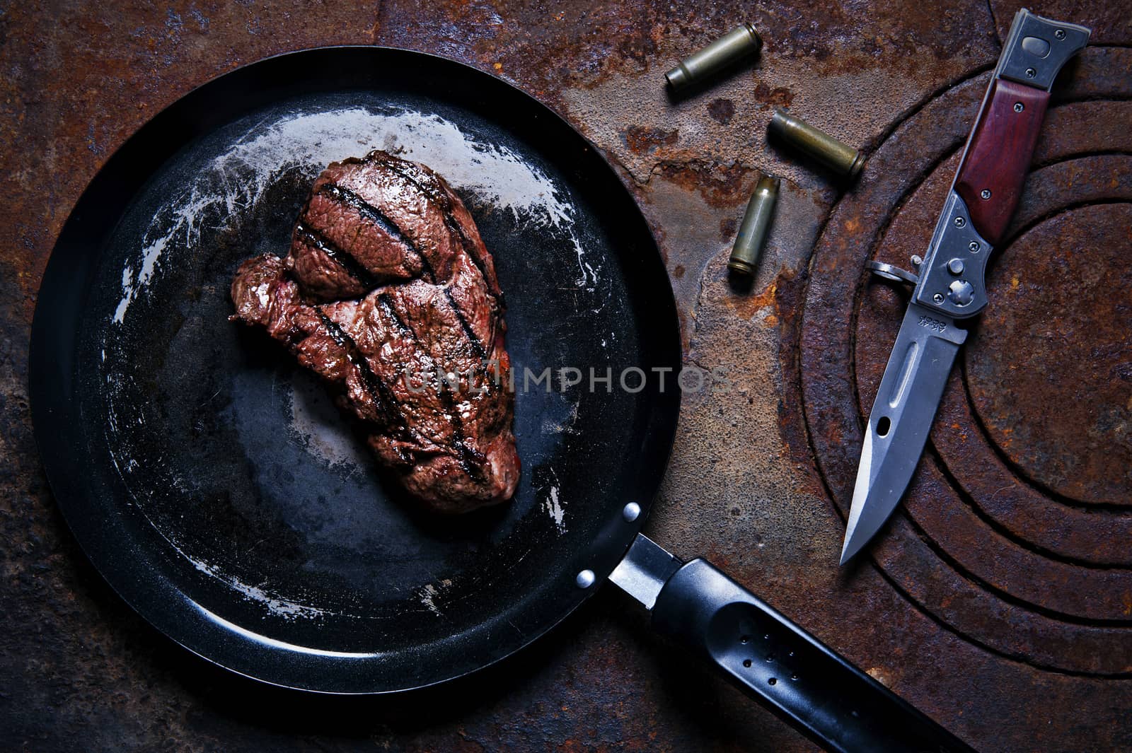 Beef steak in a frying pan standing on the rusty burner by Michalowski