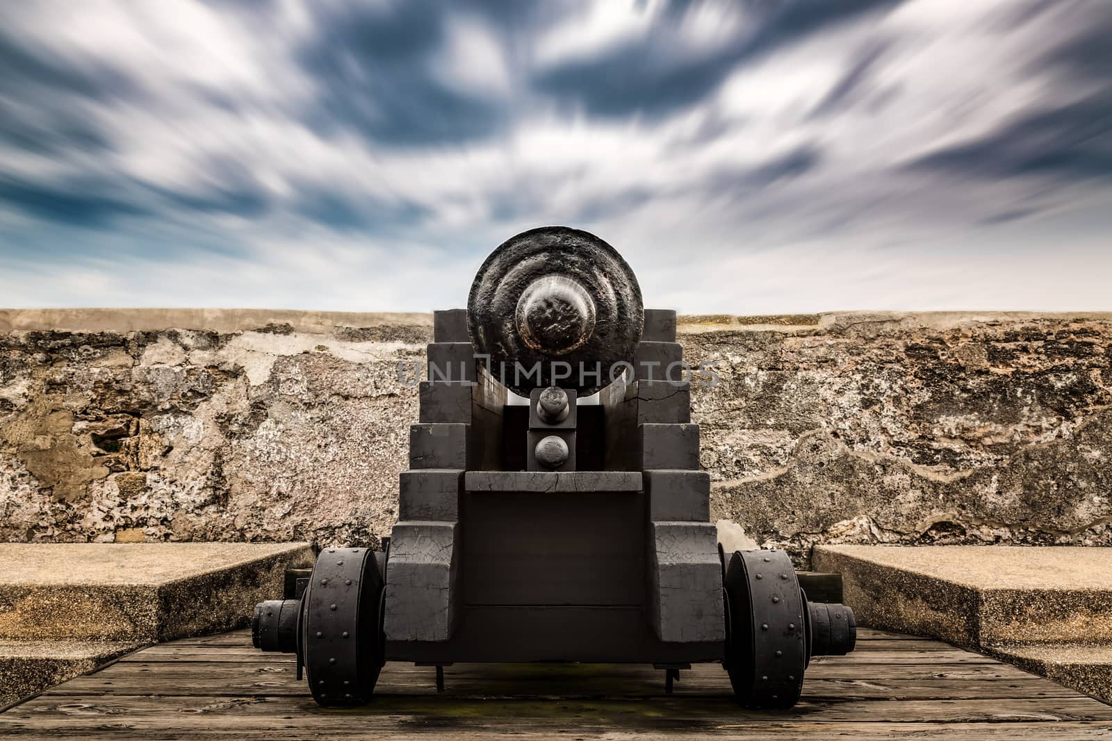 An antique cannon seen from behind under blurred skies.