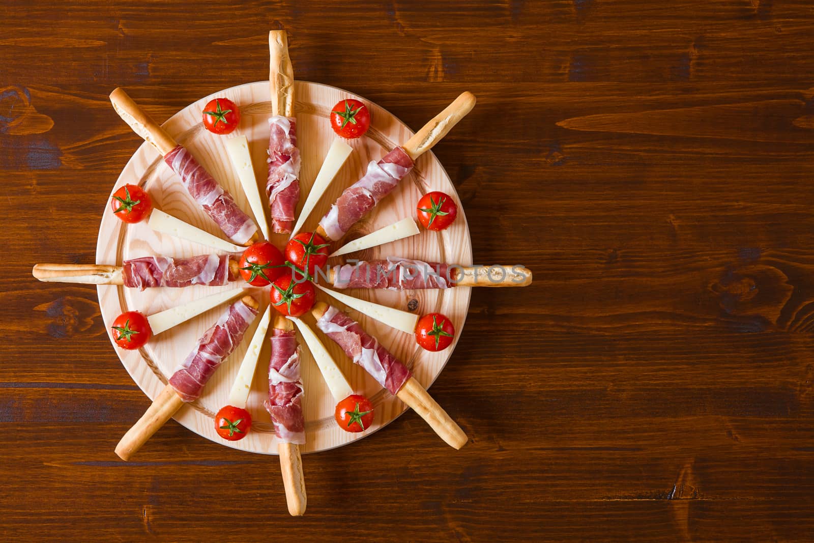 Cutting board with ham rolled in bread-sticks cheese and cherry tomatoes seen from above