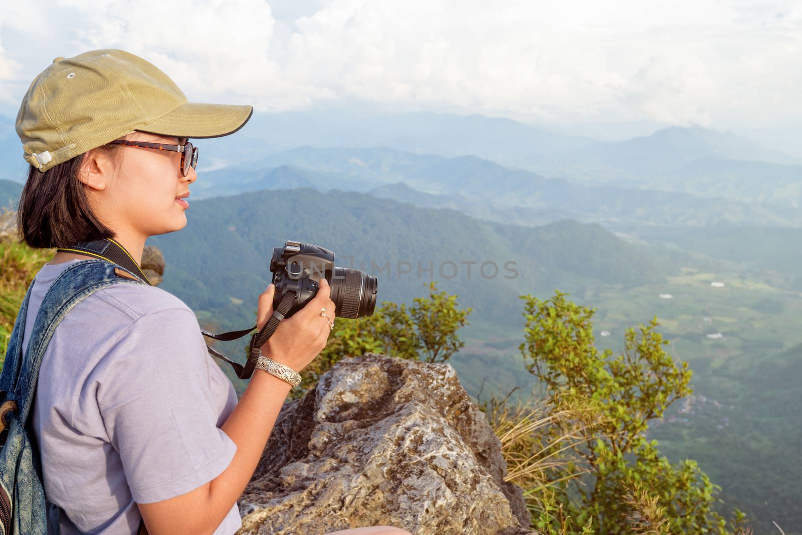 Hiker asian teen girl wear cap and eyeglass with happy holding dslr camera for photography beautiful natural in winter on peak mountain at Phu Chi Fa Forest Park, Chiang Rai, Thailand