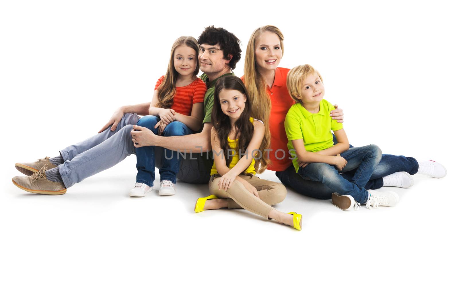 Portrait of happy family with three children sitting on the floor at studio isolated on white background