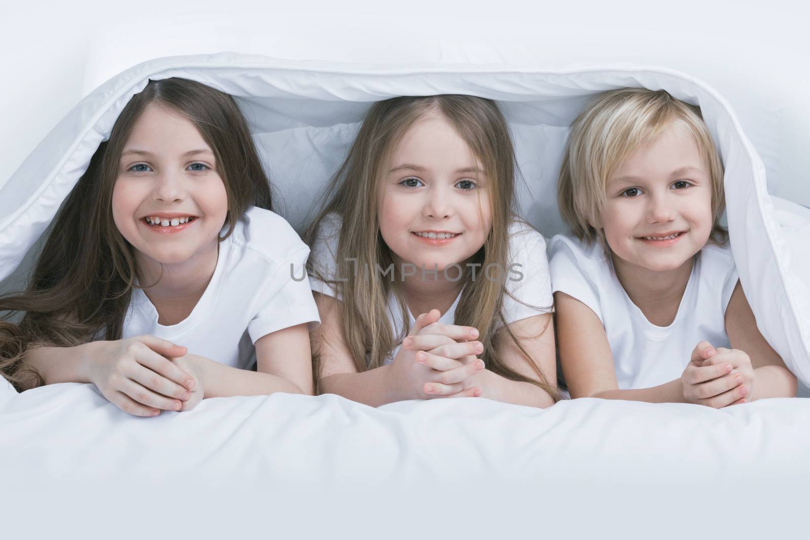 Three happy smiling children under blanket at home