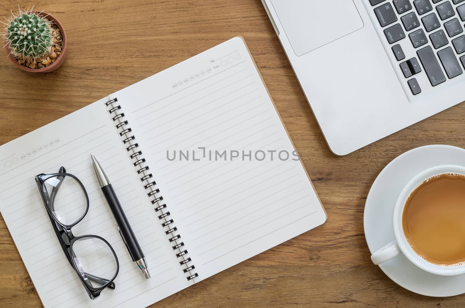 Wooden desk table with notebook, computer laptop, pen, eyeglasses, cactus and cup of coffee. Top view with copy space, flat lay.