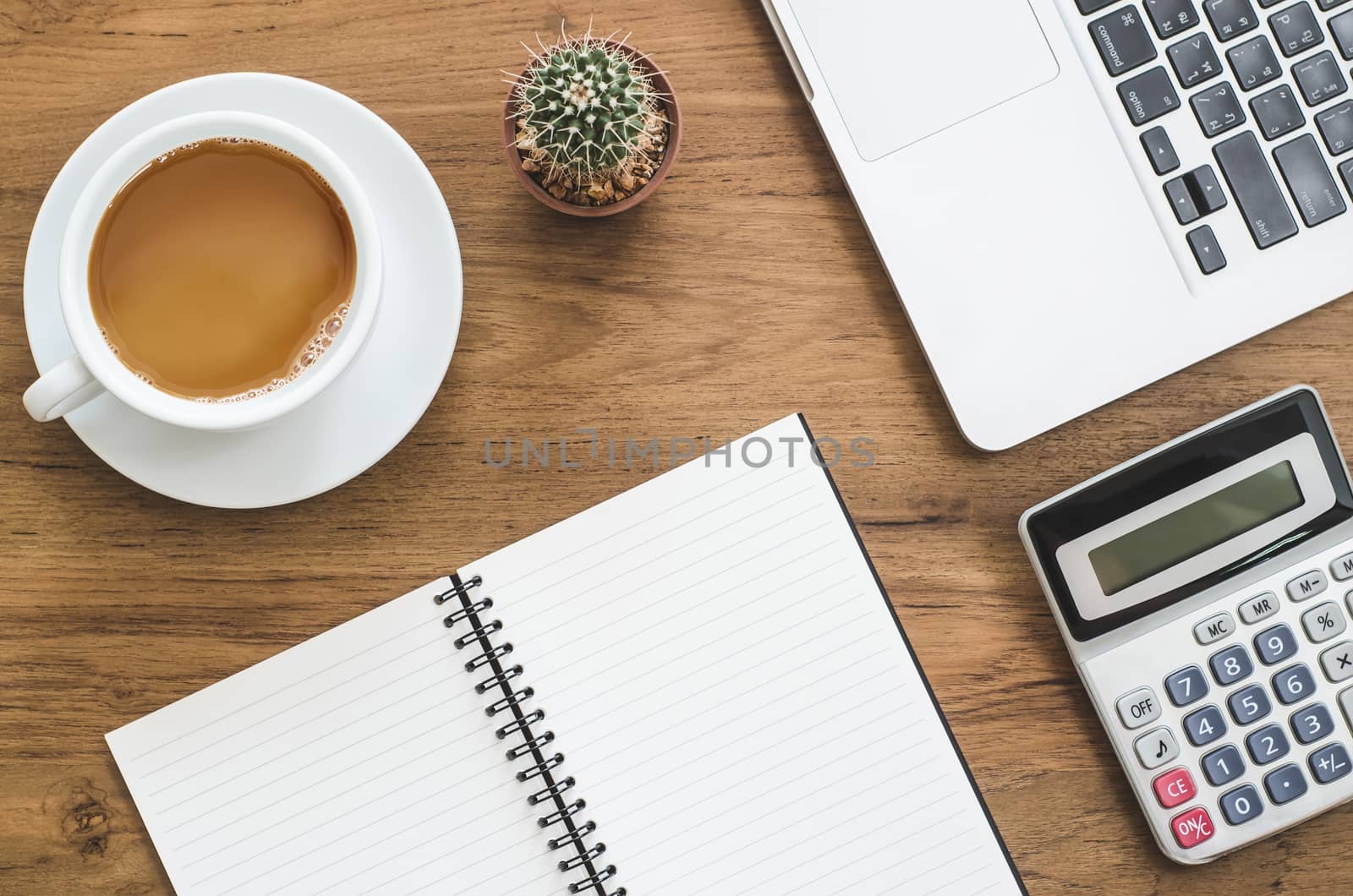 Wooden desk table with notebook, computer laptop, calculator, cactus and cup of coffee. Top view with copy space, flat lay.