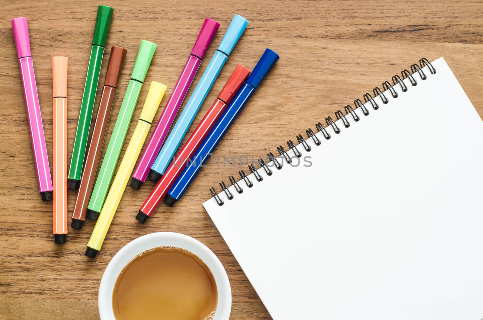 Wooden desk table with notebook, color pens and cup of coffee. Top view with copy space, flat lay.