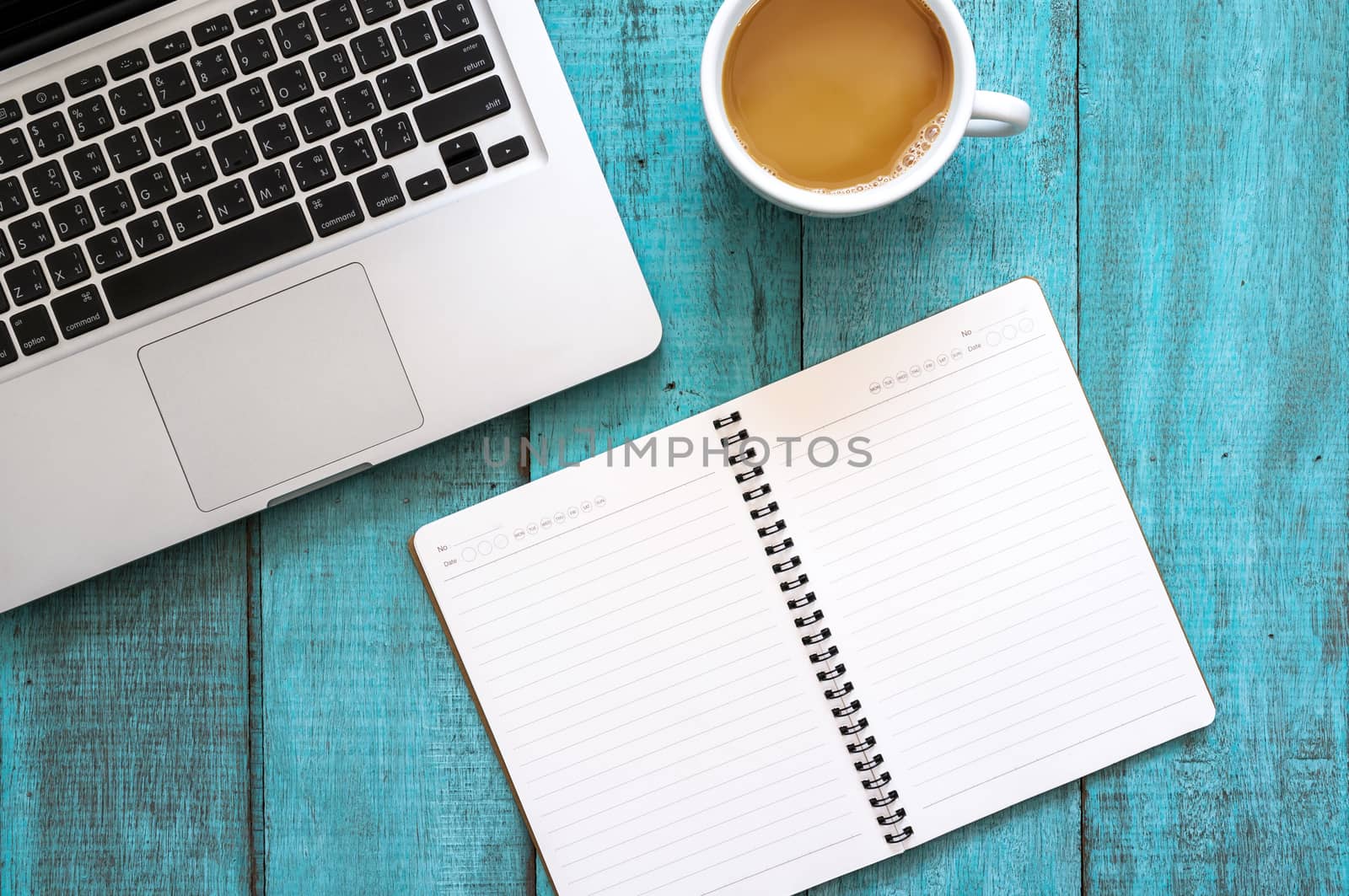 Blue wooden desk table with computer laptop, notebook and cup of coffee. Top view with copy space, flat lay.