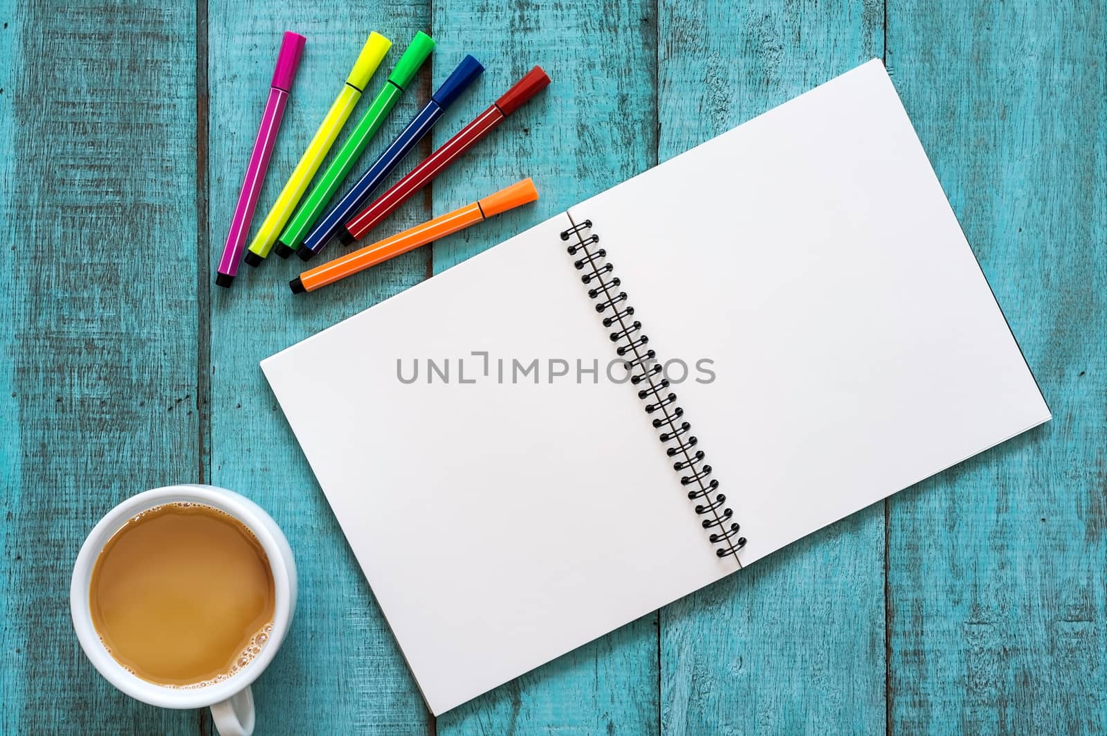 Blue wooden desk table with notebook, color pen and cup of coffee. Top view with copy space, flat lay.