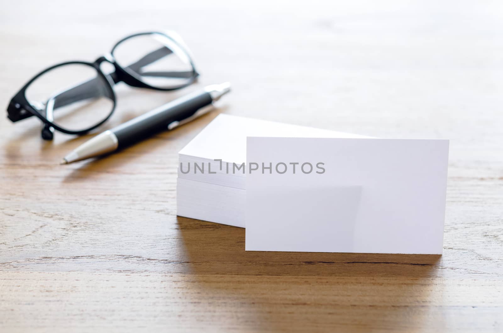 Blank business cards, pen and eyeglasses on wooden table.