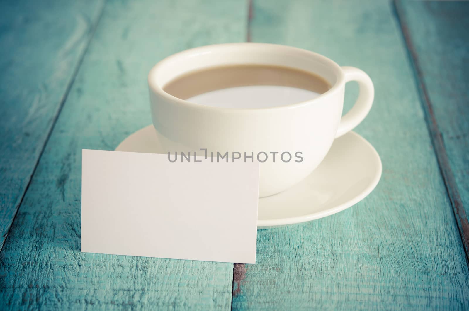 Blank business card and cup of coffee on blue wooden table. Vintage filter.