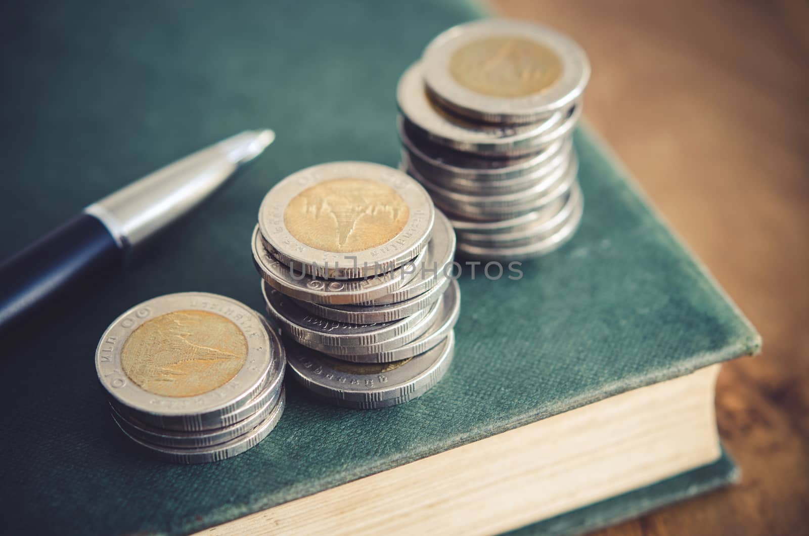 Business concept. Closeup stack of coins, pen and old book on ta by koson