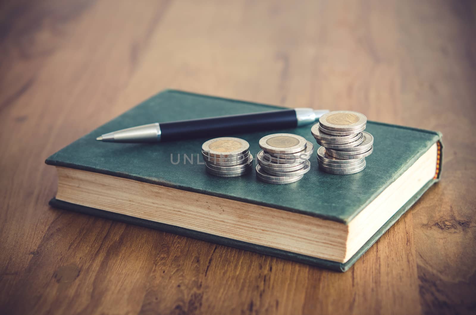 Business concept. Closeup stack of coins, pen and old book on wooden table.