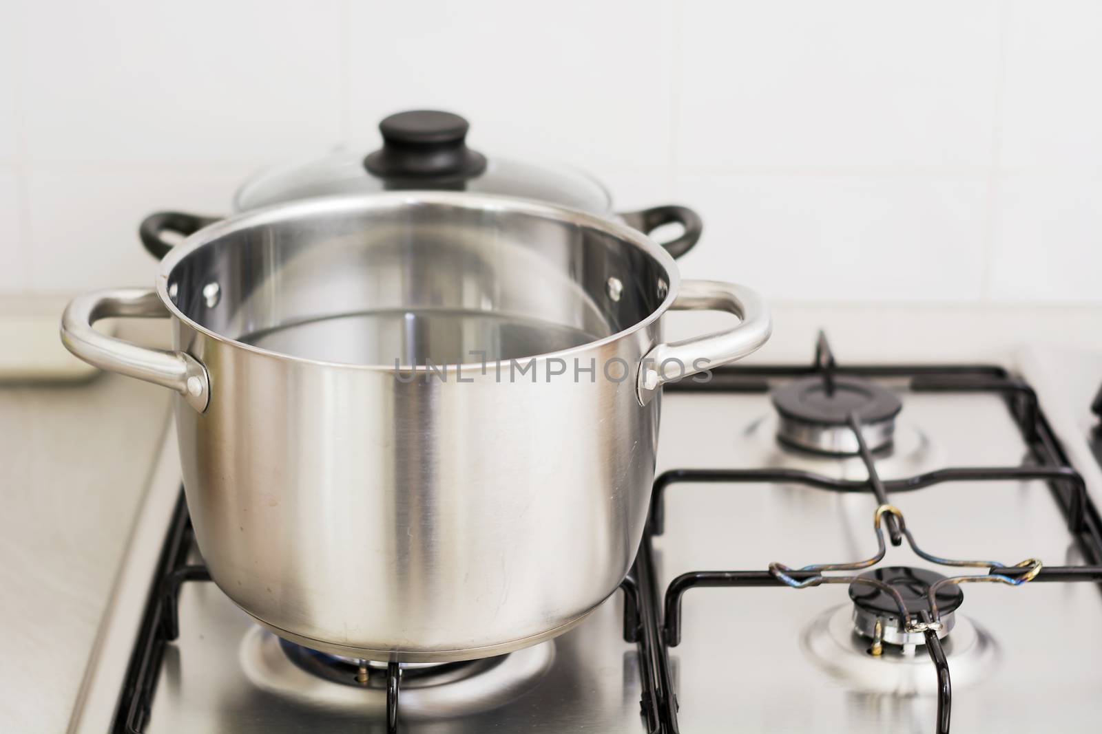 Close-up of stainless steel cooking pot on gas stove in contemporary upscale modern home kitchen. Selective focus on pot.