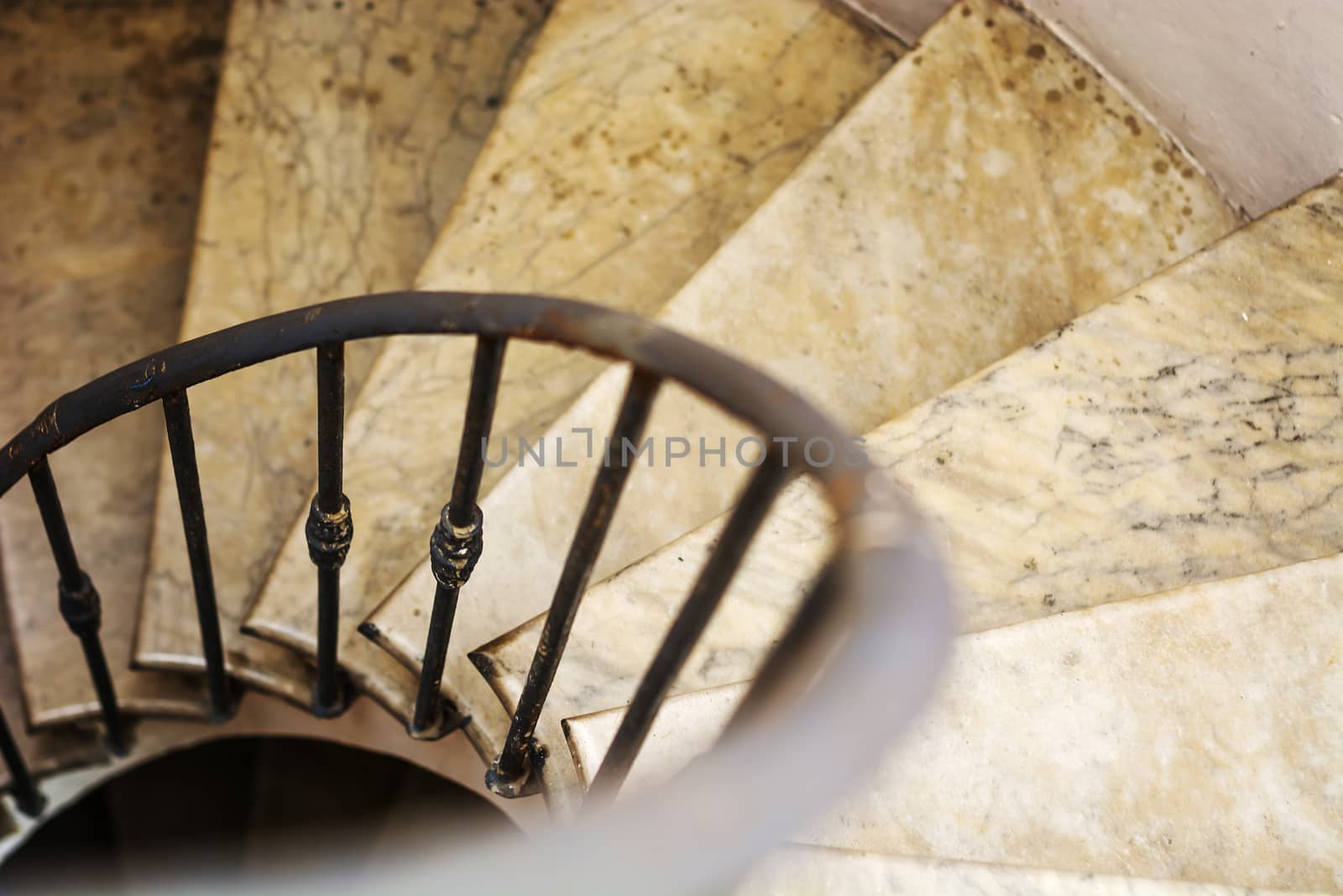 Upside view of indoor spiral winding staircase with black metal ornamental handrail.