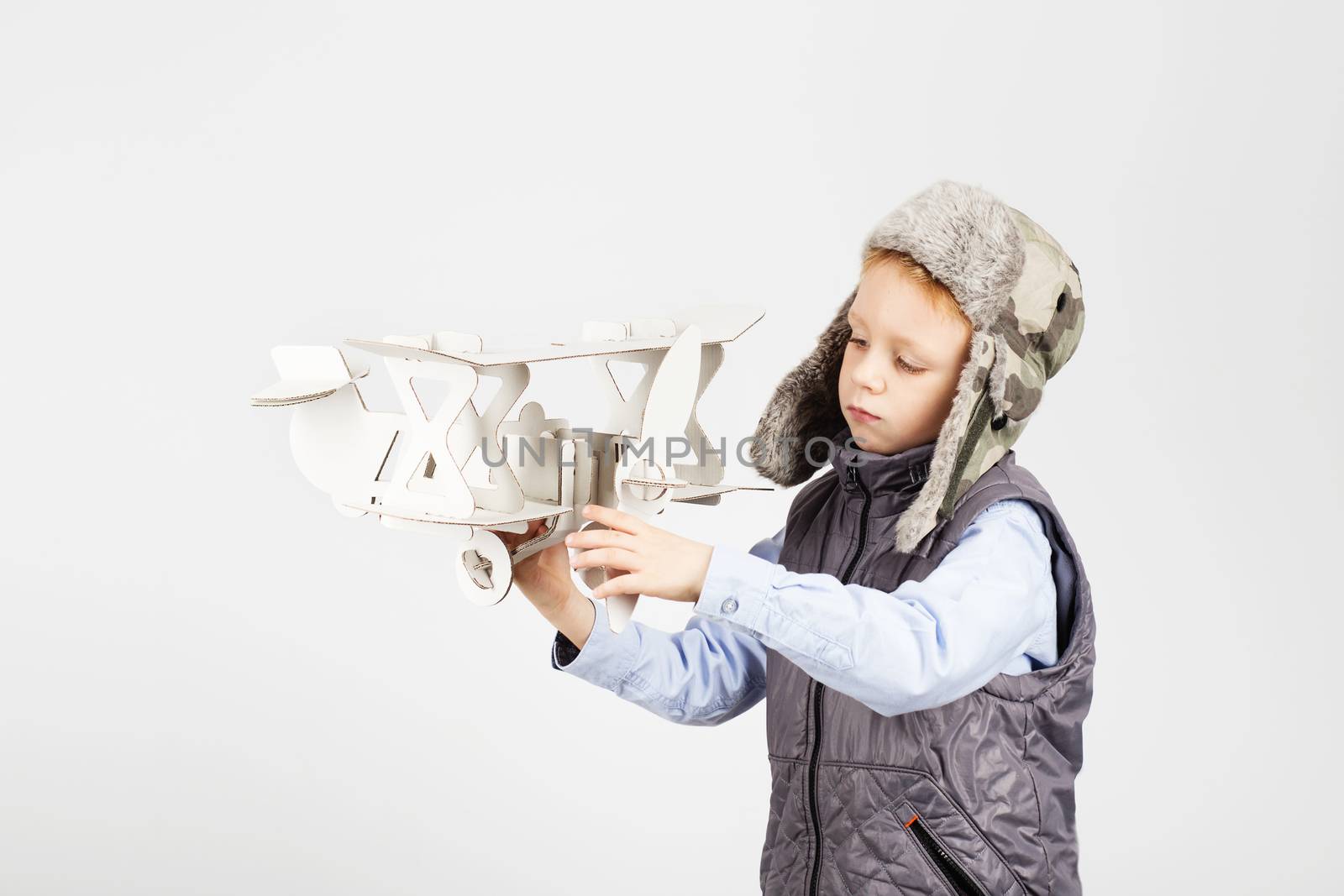 Child boy playing with paper toy airplane and dreaming of becoming a pilot against a white background