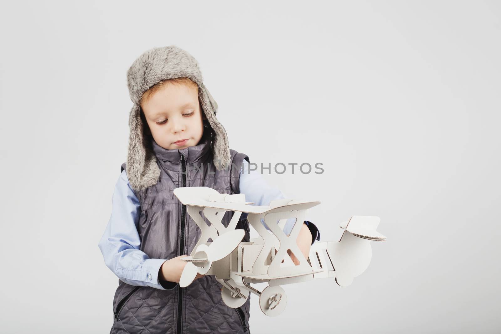 Child boy playing with paper toy airplane and dreaming of becoming a pilot against a white background
