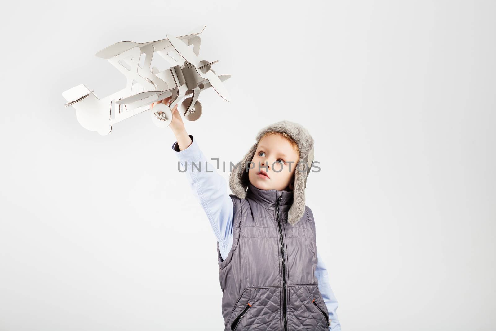 Child boy playing with paper toy airplane and dreaming of becoming a pilot against a white background