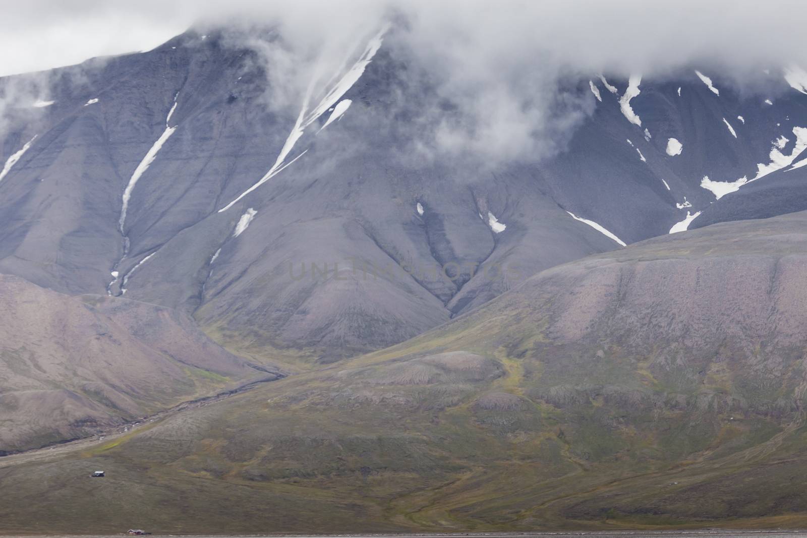 Beautiful scenic view of blue gulf under barren mountain range with melting snow against the background of dramatic evening sky near Barentsburg, Spitsbergen (Svalbard island), Norway, Greenland sea

