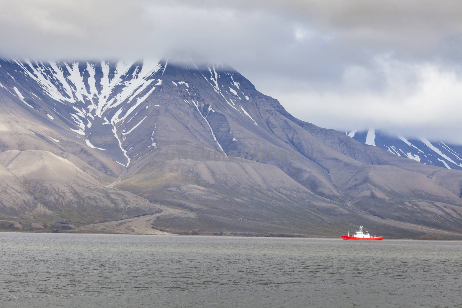 Beautiful scenic view with norge cruise boat docked at Longyearbyen port against the background of fogged black mountain and calm water of Advent Bay, Spitsbergen (Svalbard), Norway, Greenland sea

