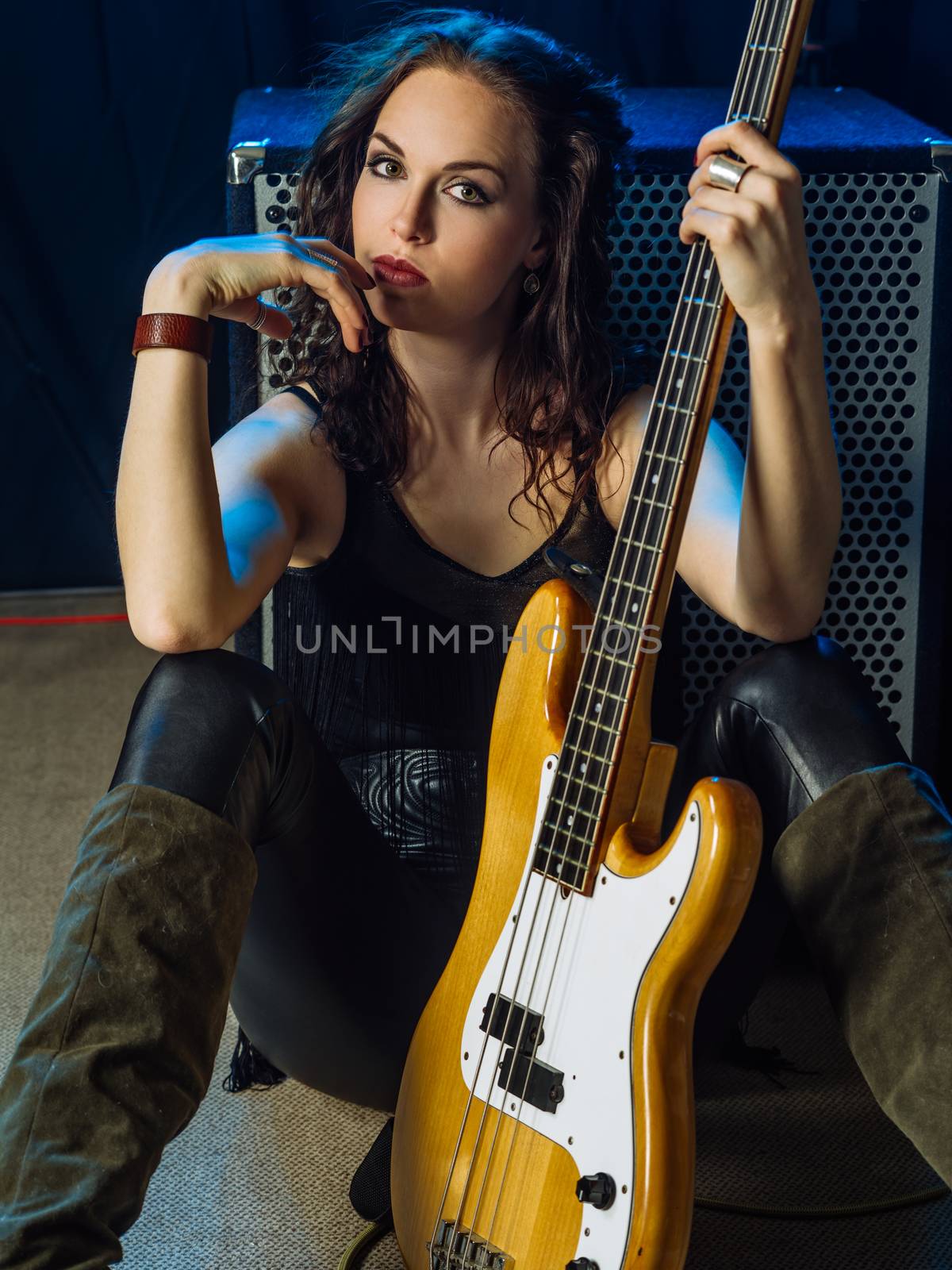 Photo of a beautiful woman bass player sitting in front of her amplifier.