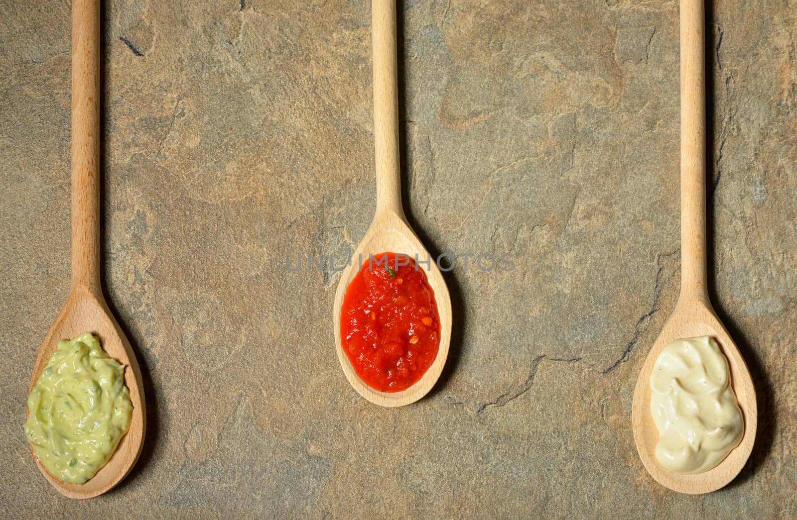 different types of sauces in spoons on stone table