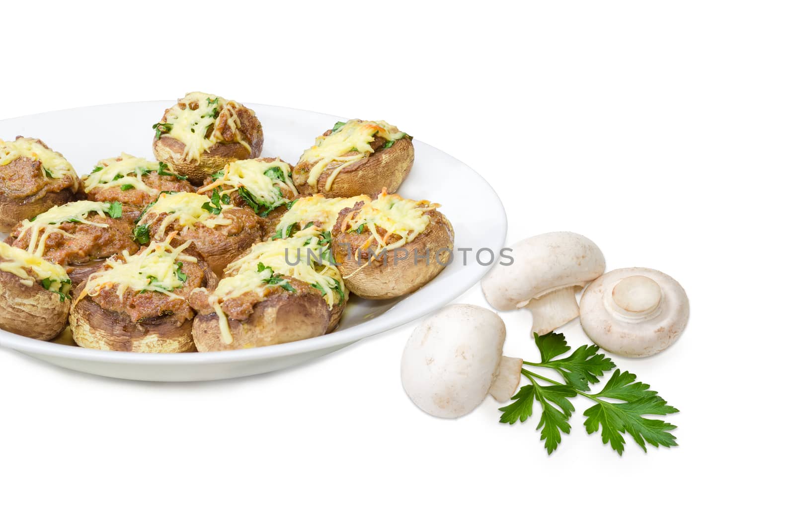 Baked button mushrooms stuffed with minced meat, cheese and greens on the white dish and several uncooked mushrooms with parsley twig beside closeup on a light background
