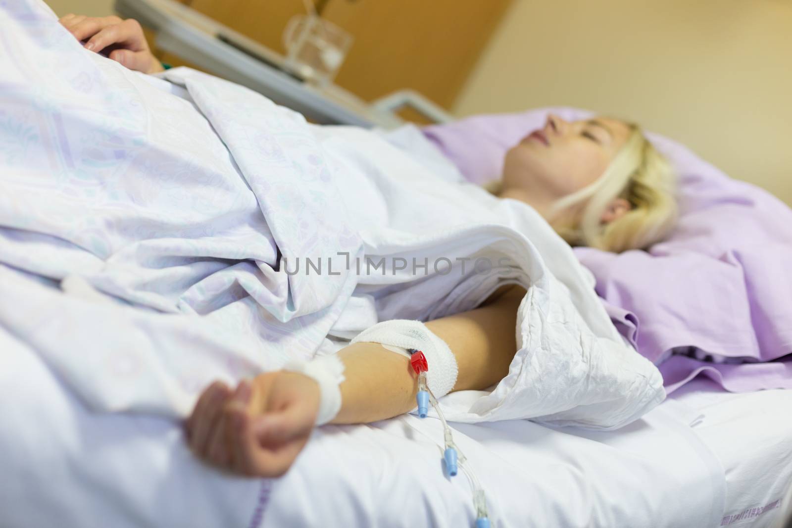 Bedridden female patient lying in hospital bed, receive infusion while recovering after surgery.