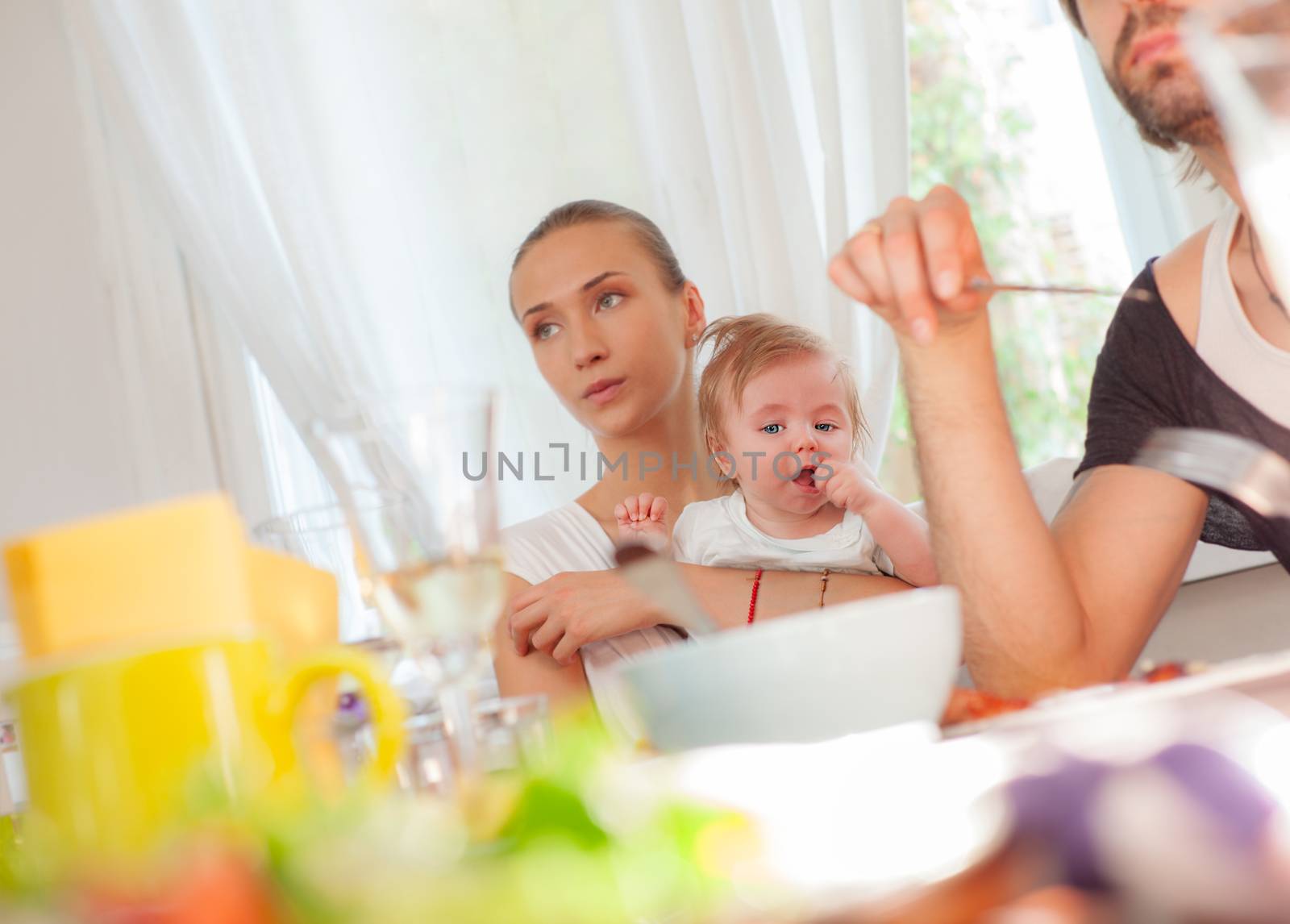 A little baby boy is held by his mother in restaurant during a family lunch.