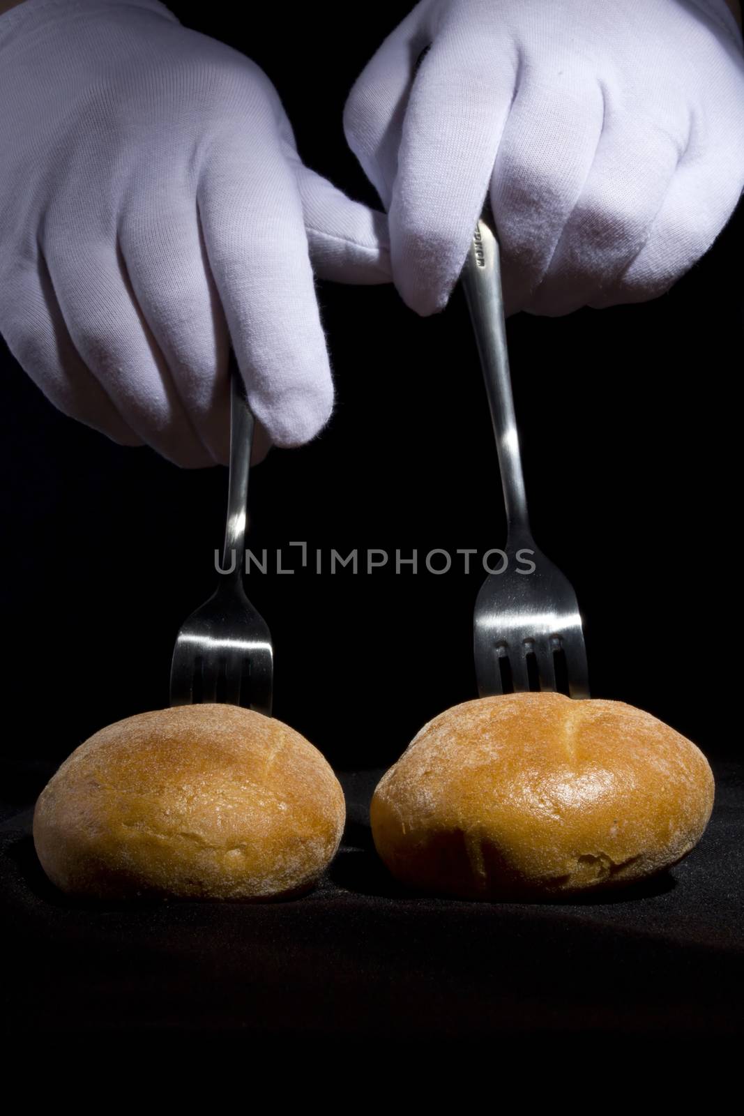 Buns on the forks and hands in white gloves on a black background