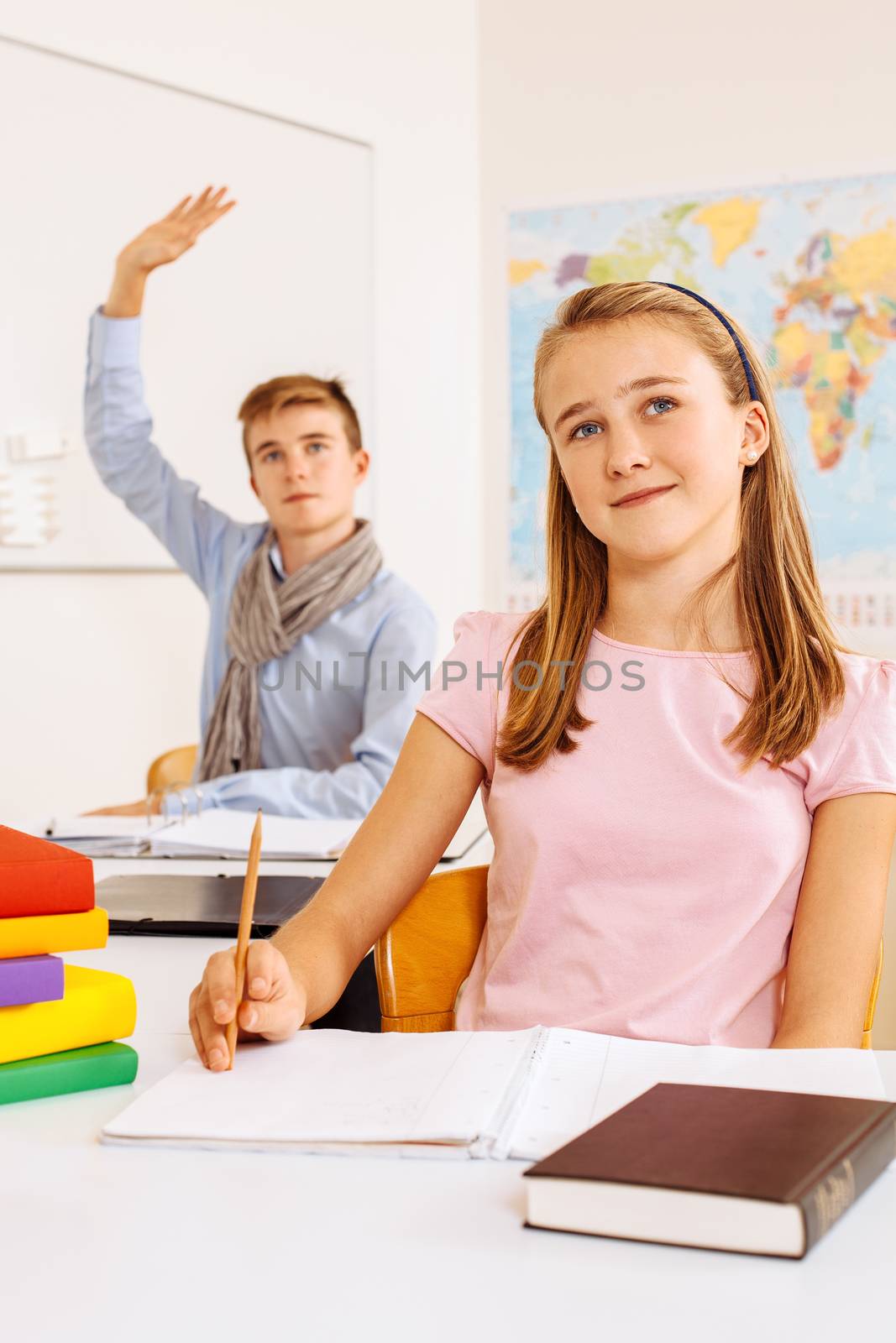 Photo of two teenagers in a classroom happy and lifting their hands to answer a question.